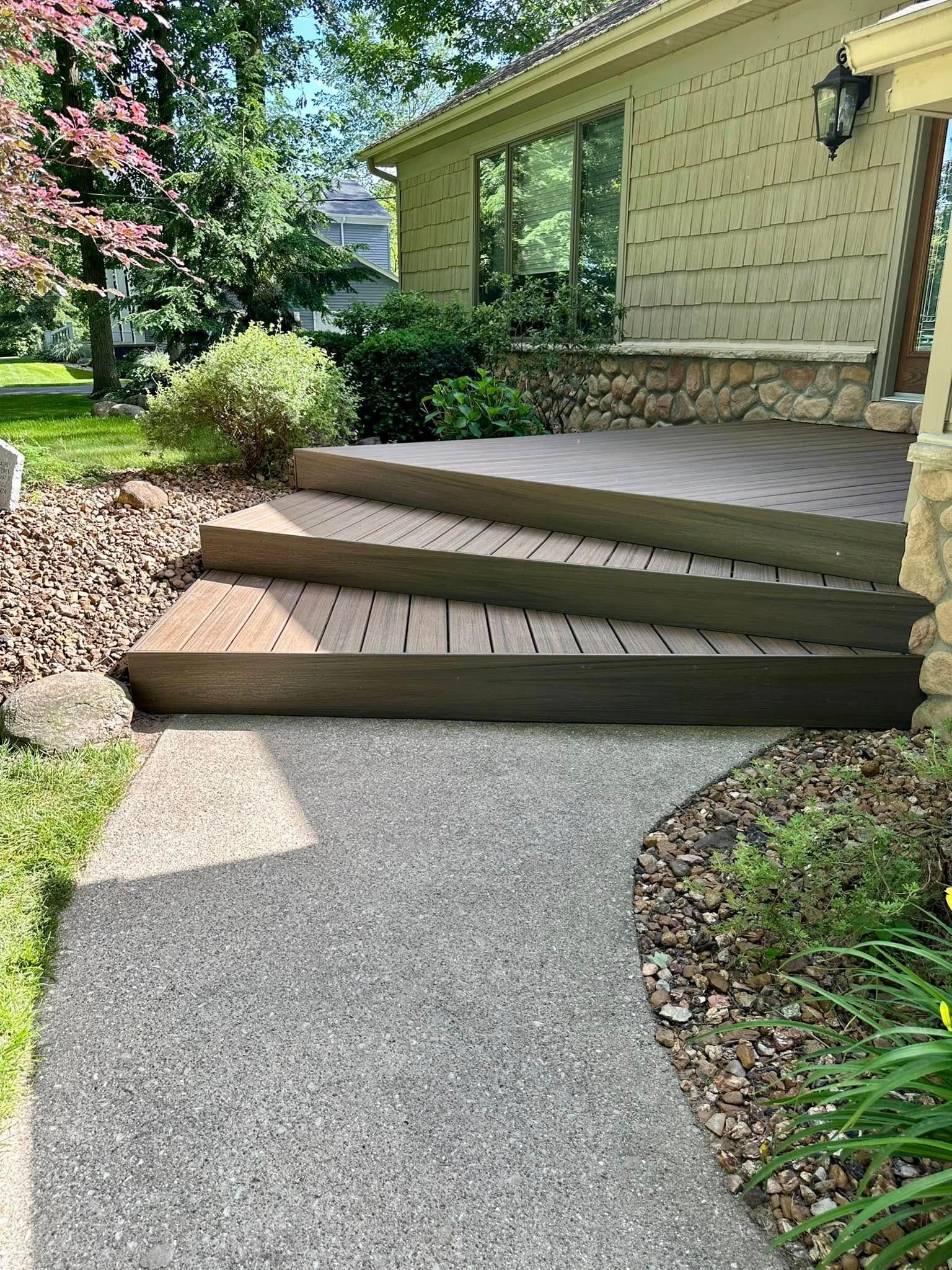 Three brown composite steps lead to a house entrance. A gray concrete path is in the foreground.