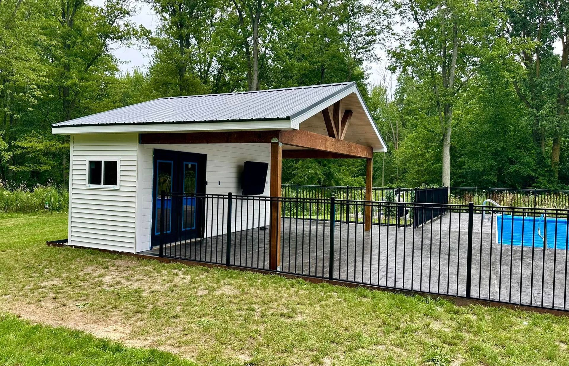 Poolside shed with black fence, white siding, and a silver metal roof.