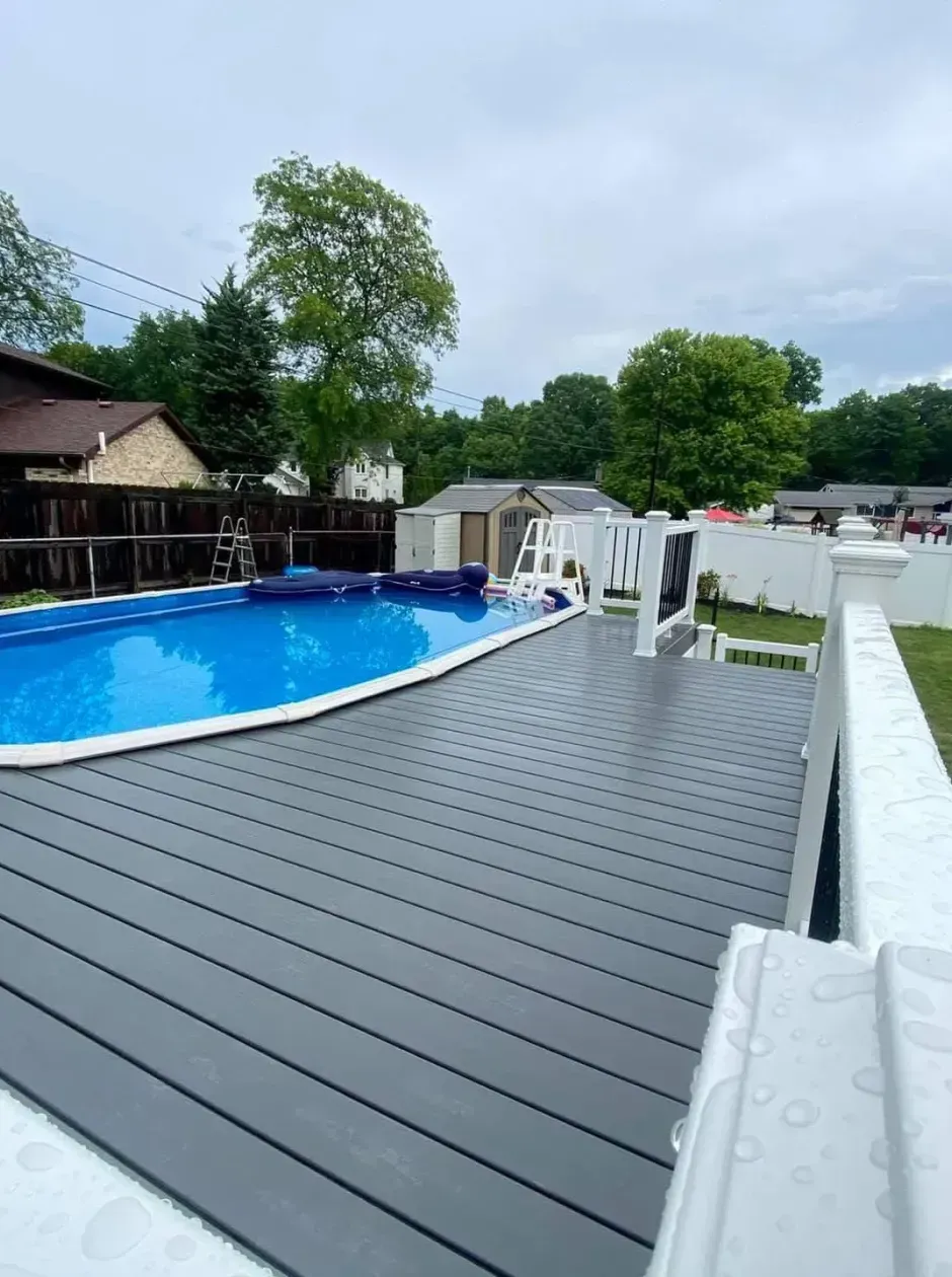 A large swimming pool is surrounded by a fence and a deck.