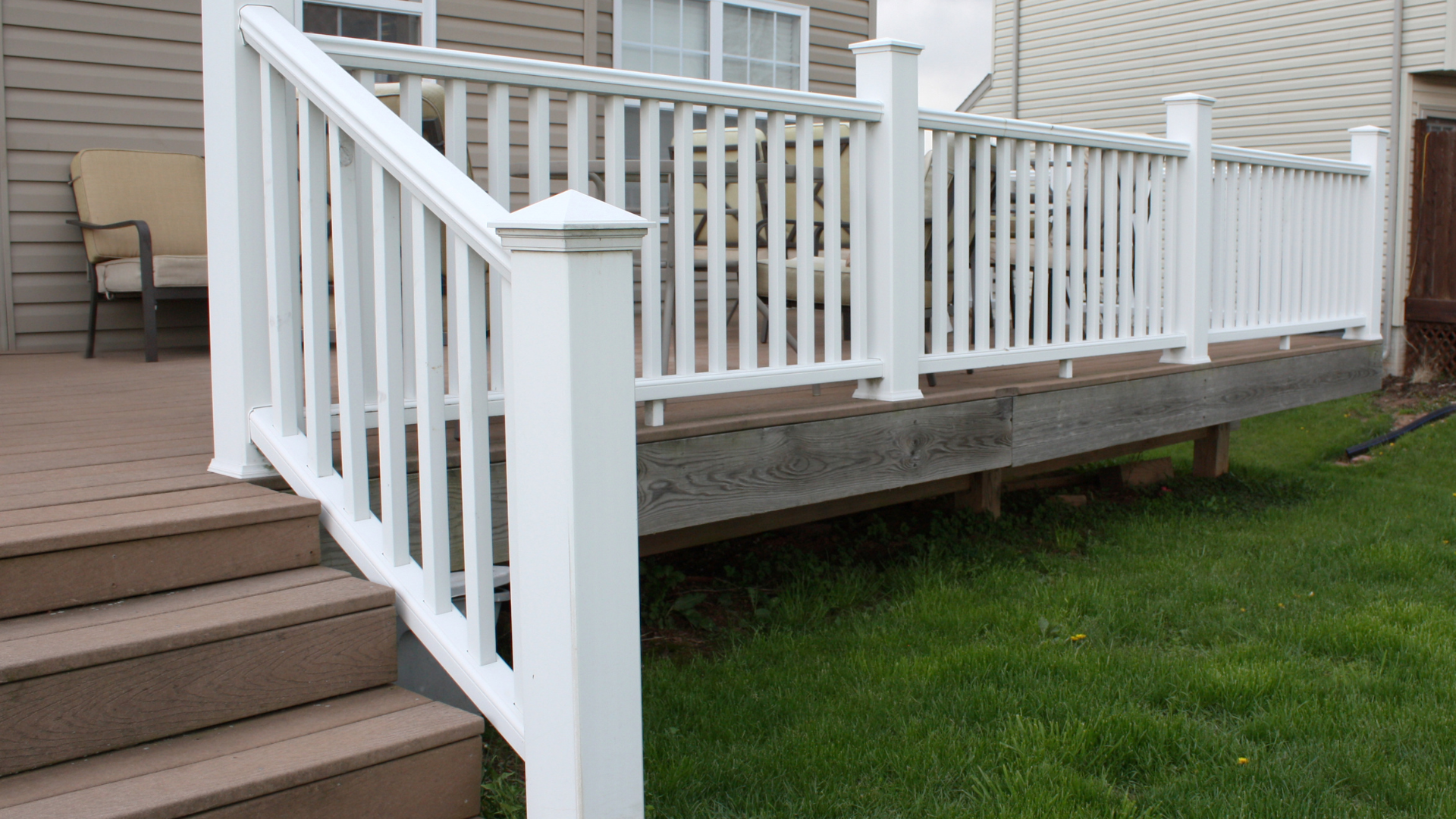 White deck railing and stairs on a wooden deck in a yard with green grass.
