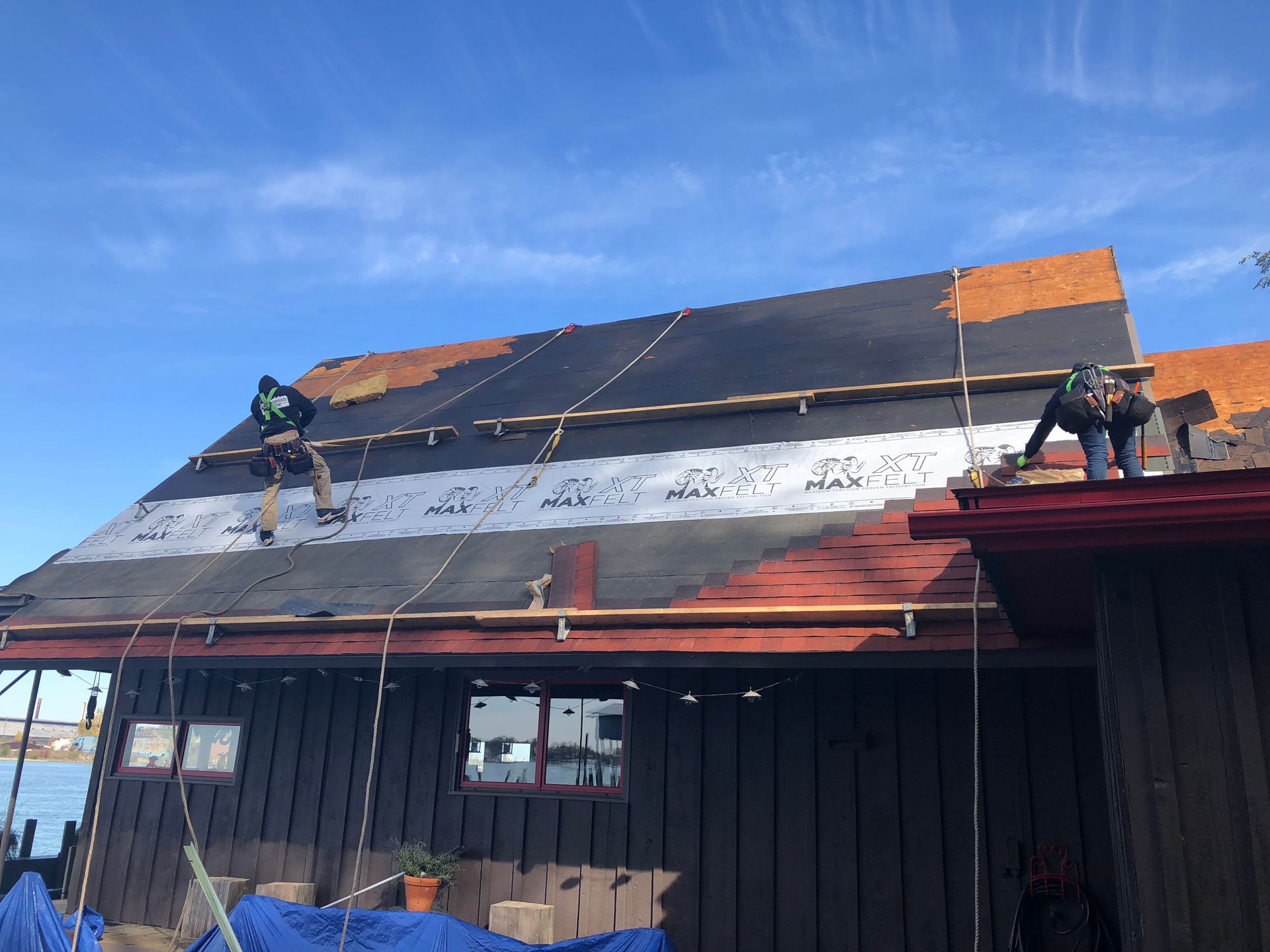 Two roofers on a rooftop, replacing shingles. The roof is partially covered with new black shingles.
