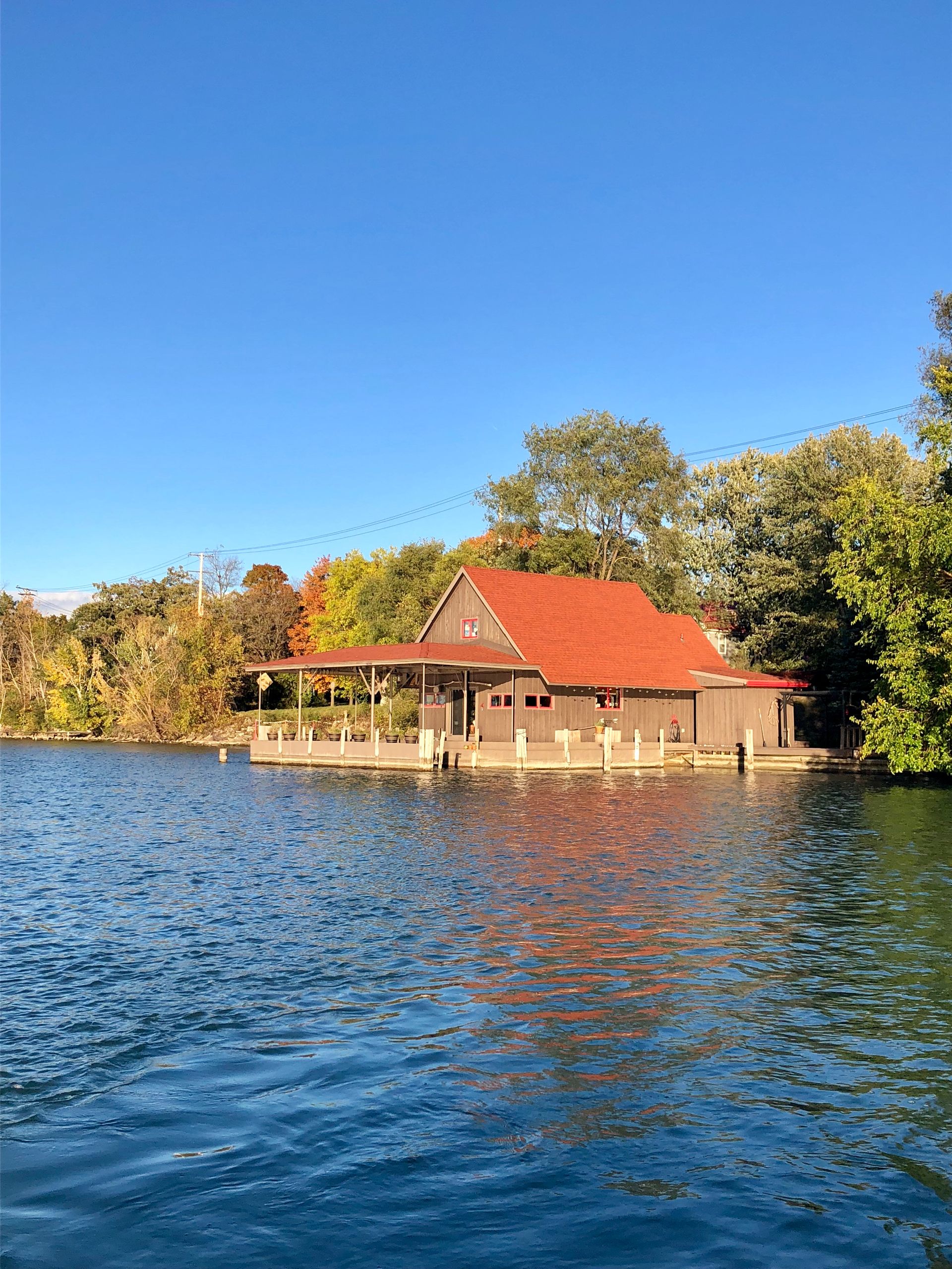 Boathouse with orange roof on lake under a blue sky, surrounded by trees.