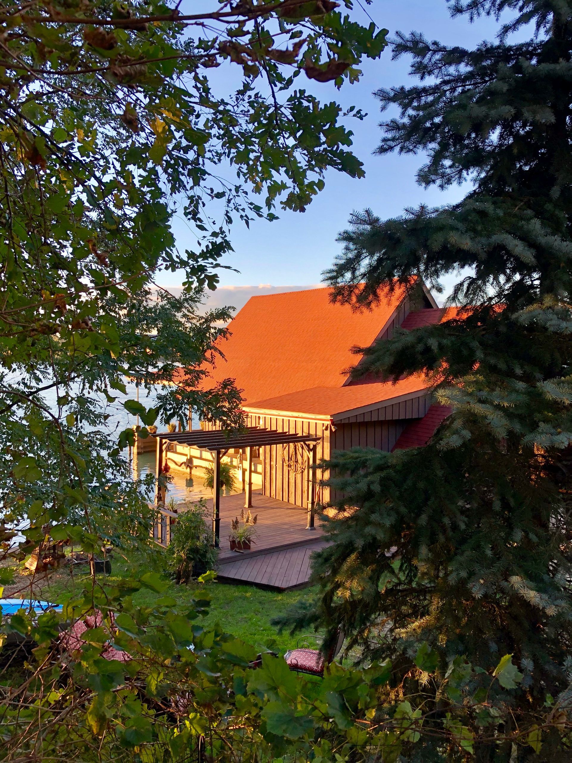 A house with a red roof, viewed through foliage, bathed in warm sunlight.