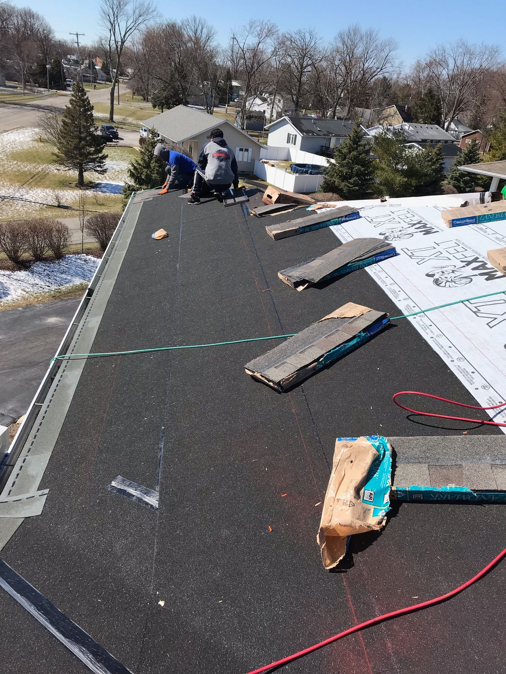 Roofers working on a black asphalt roof under a sunny sky.