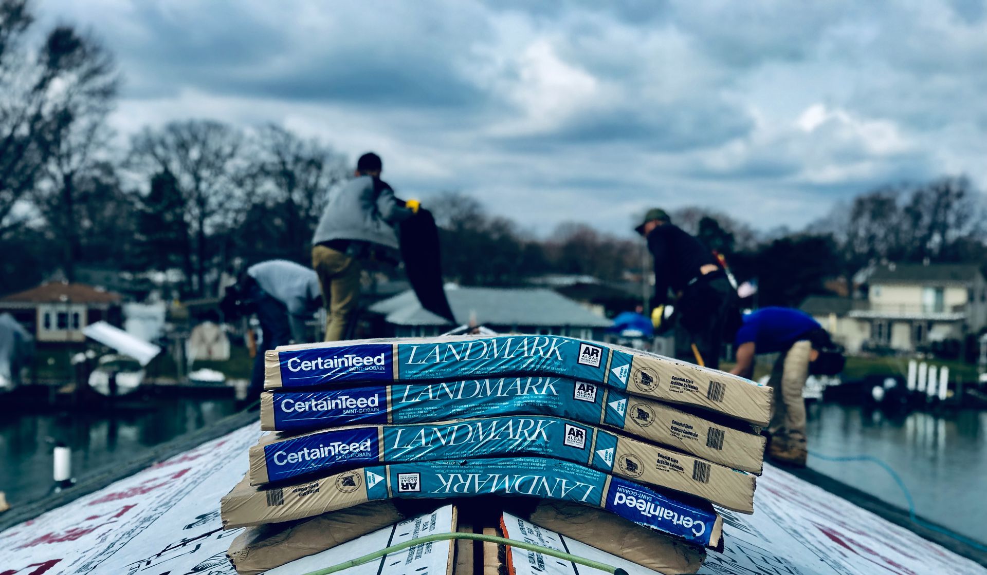 Roofers installing shingles on a house near water, cloudy day.