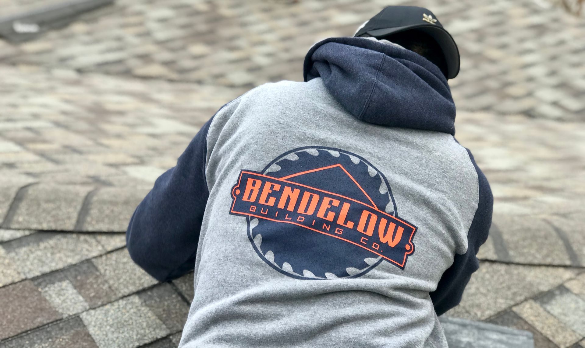 Roofer wearing a gray hoodie with a company logo on a roof.