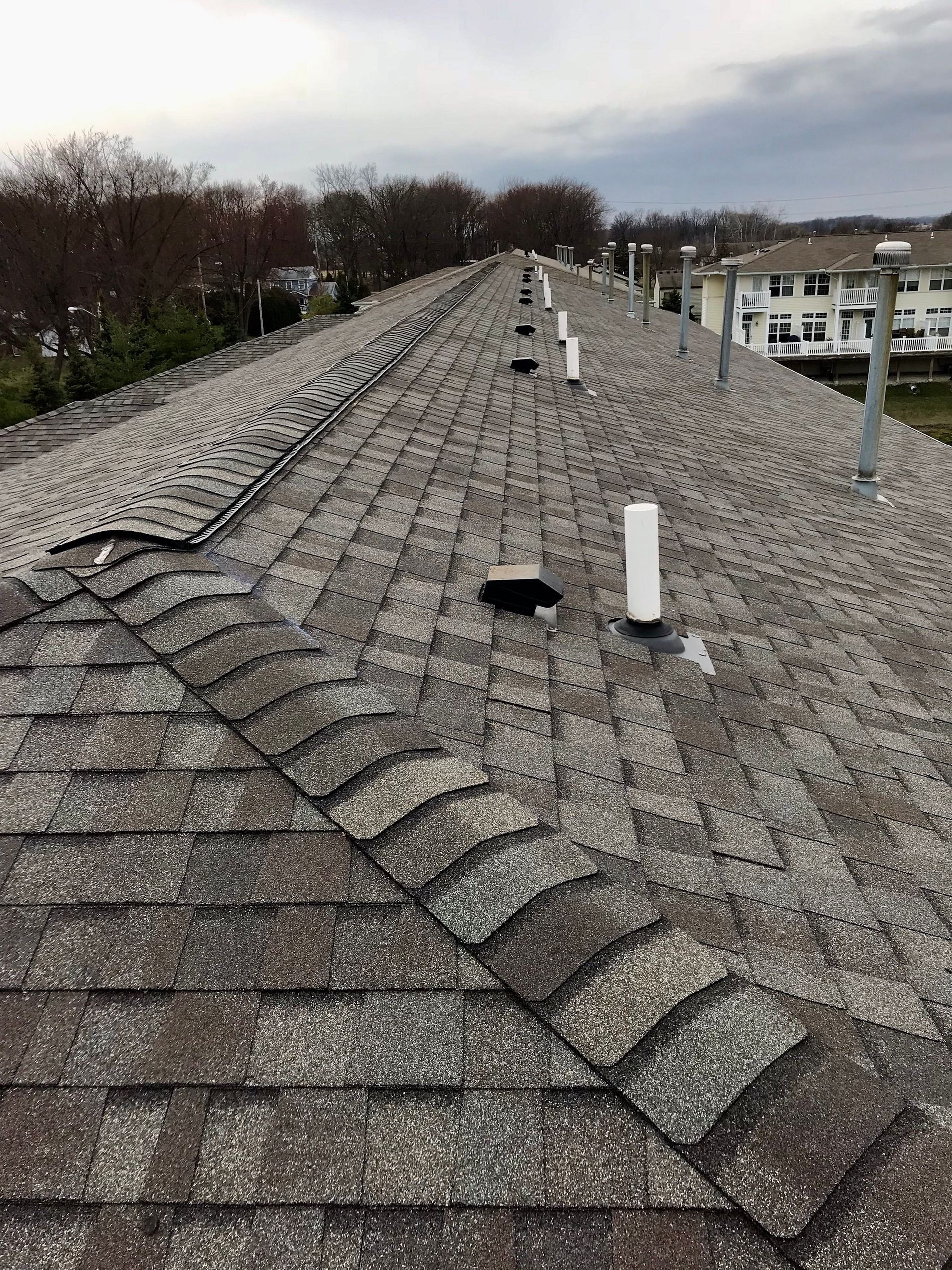 View of a weathered asphalt shingle roof with several vent pipes, against a cloudy sky.