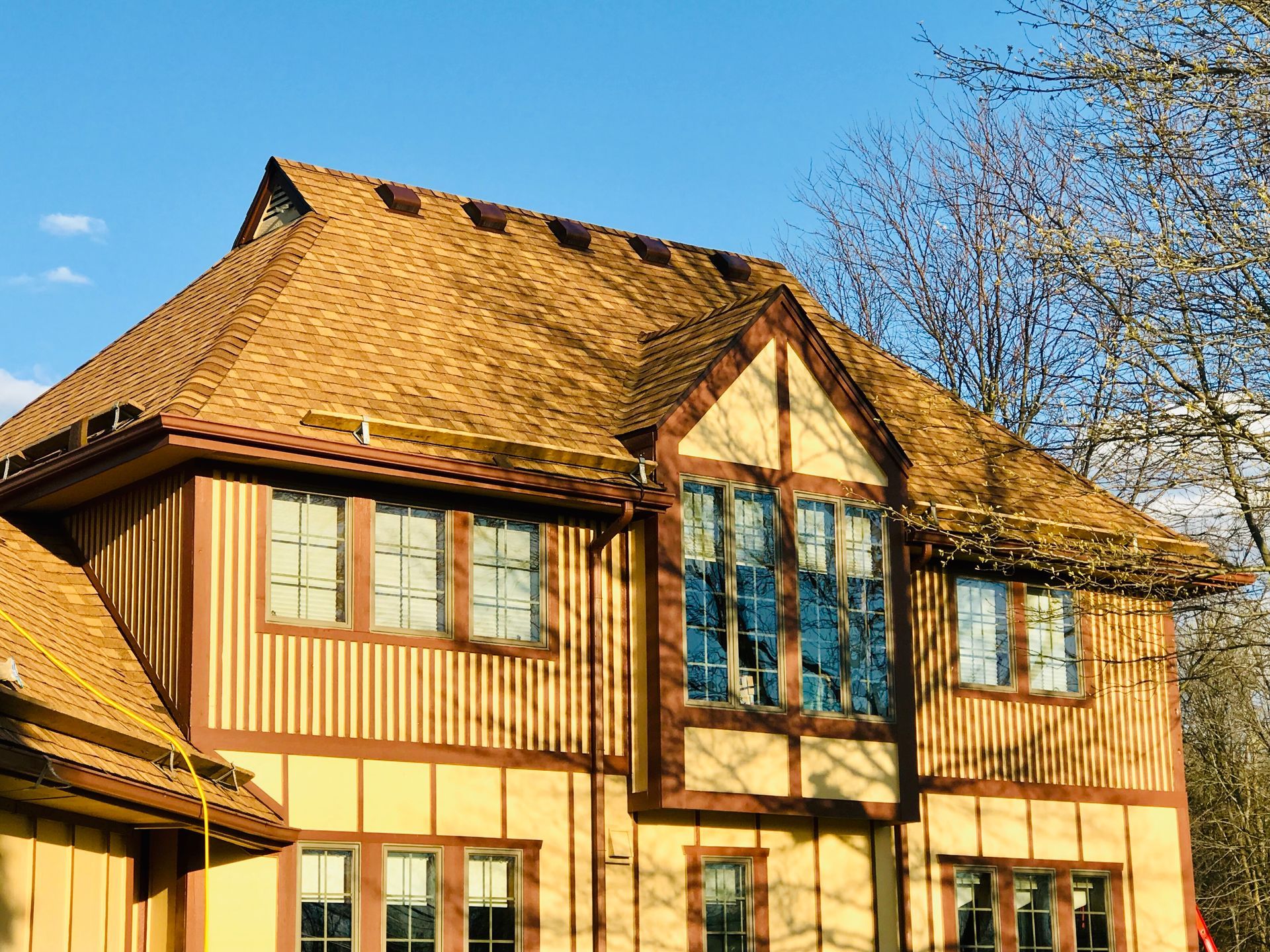 Two-story house with brown roof and beige siding against a blue sky.