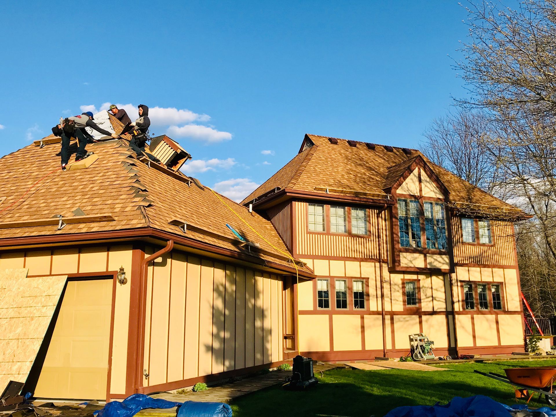 Roofers on a house with brown and beige Tudor style, blue sky.