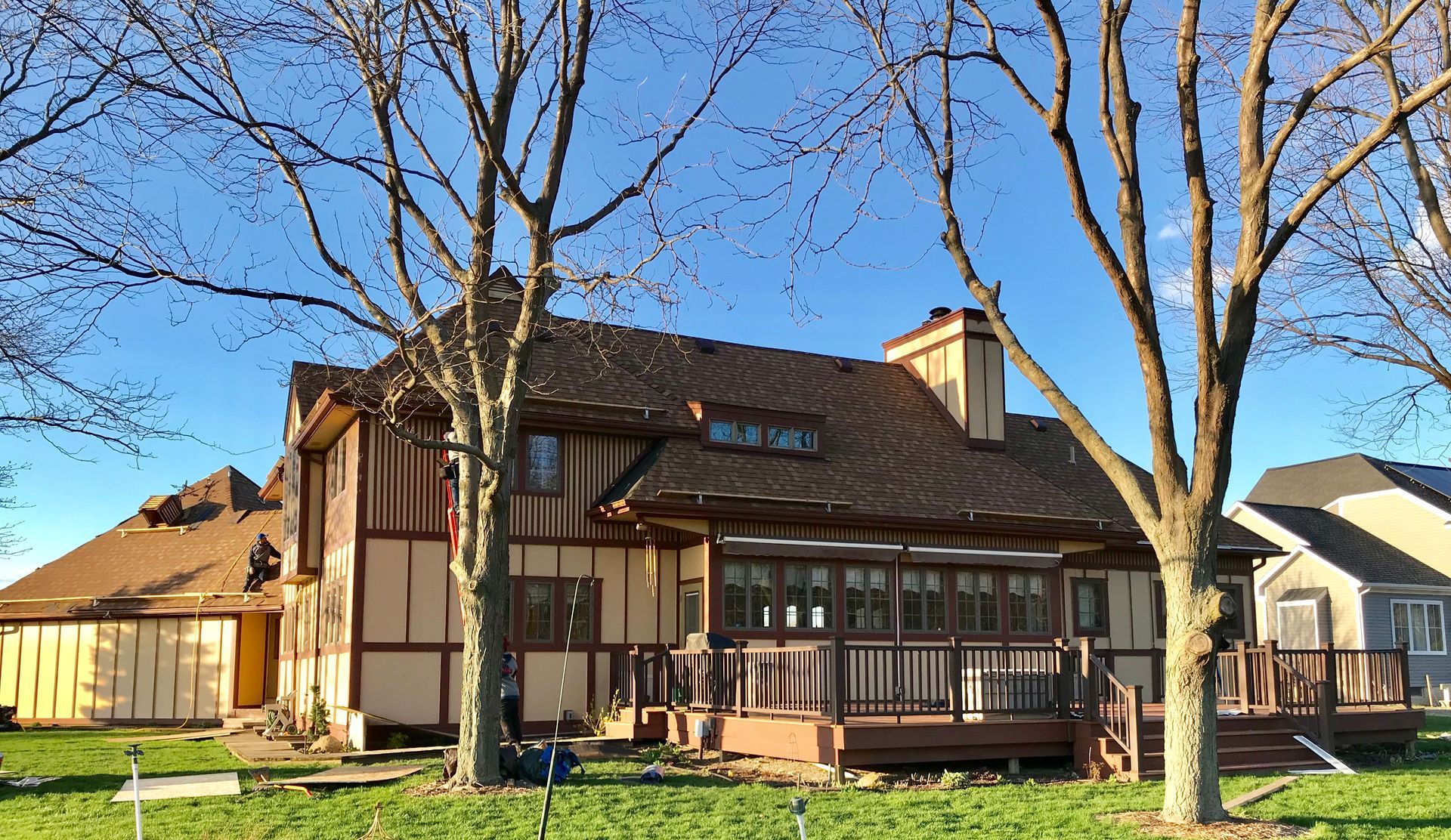 House with brown roof, wooden deck, and trees against a blue sky.