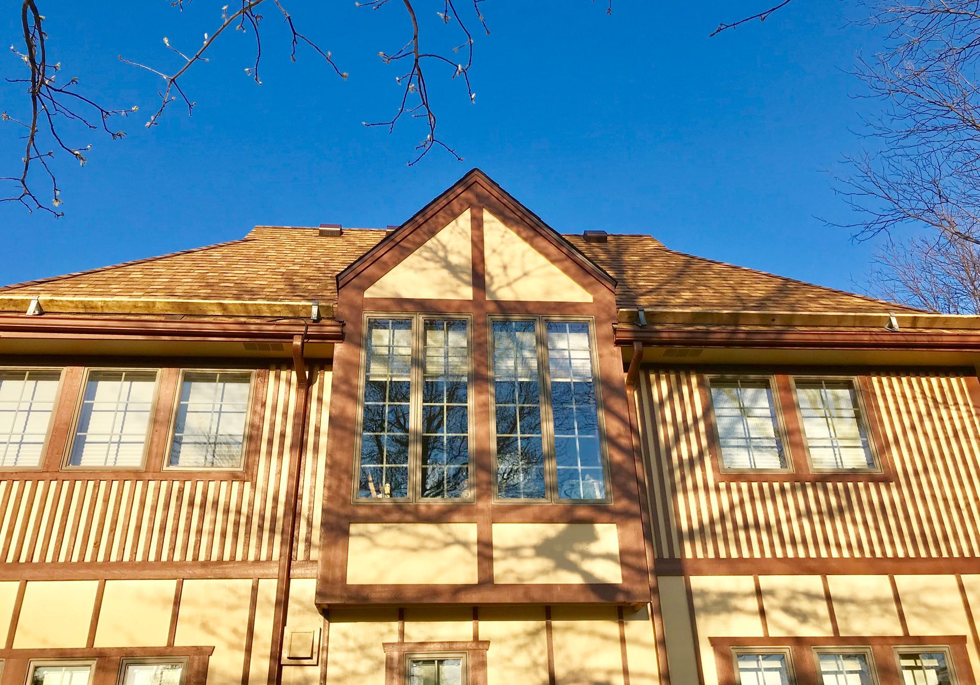 Two-story house with tan and brown Tudor-style architecture against a bright blue sky.