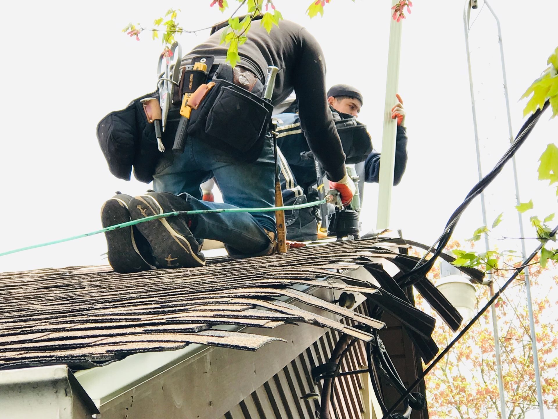 Two workers on a rooftop installing or repairing something. One kneels, the other holds a pole.