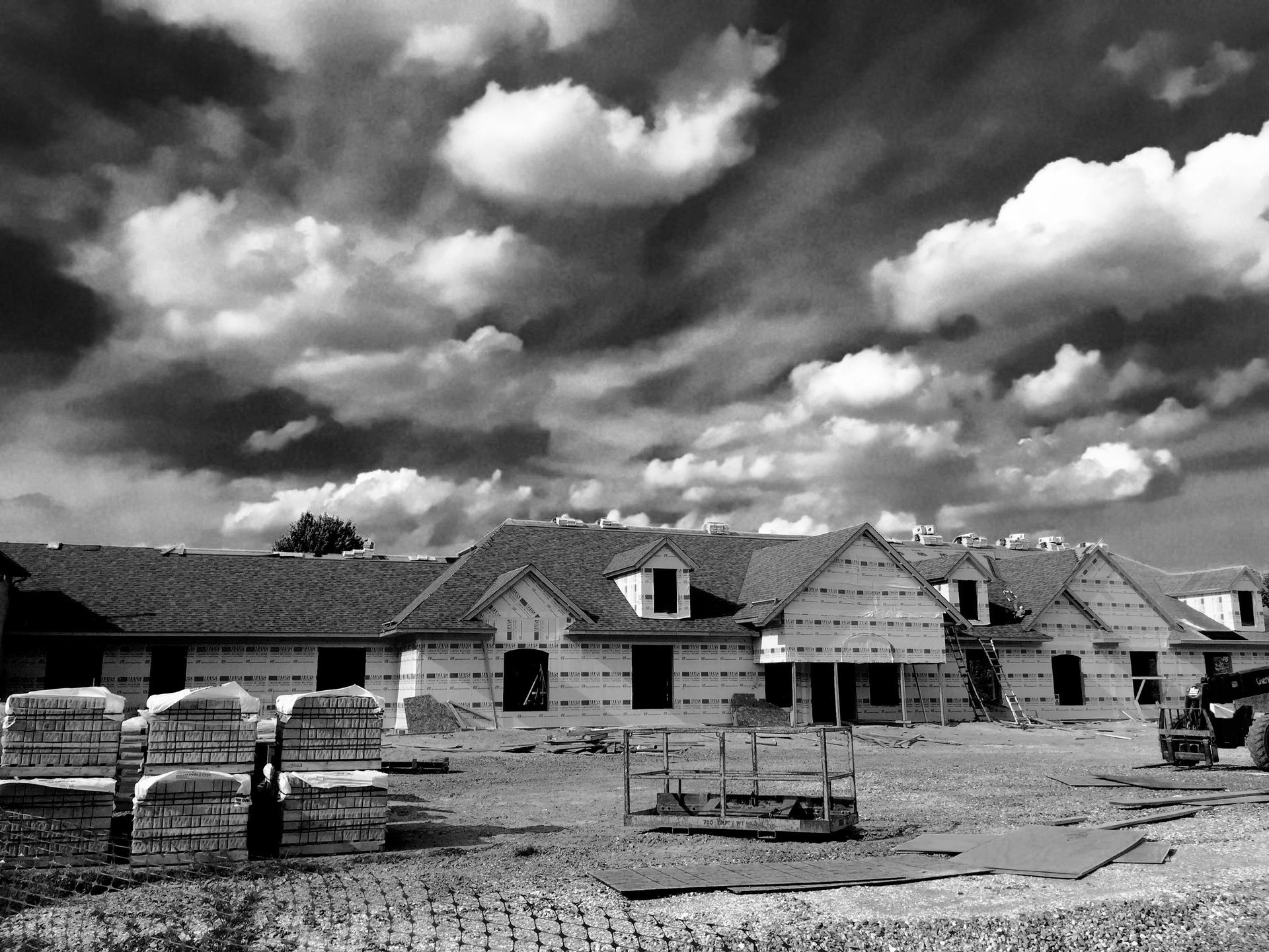 Black and white photo of a new house under construction, cloudy sky overhead, bricks and materials in foreground.
