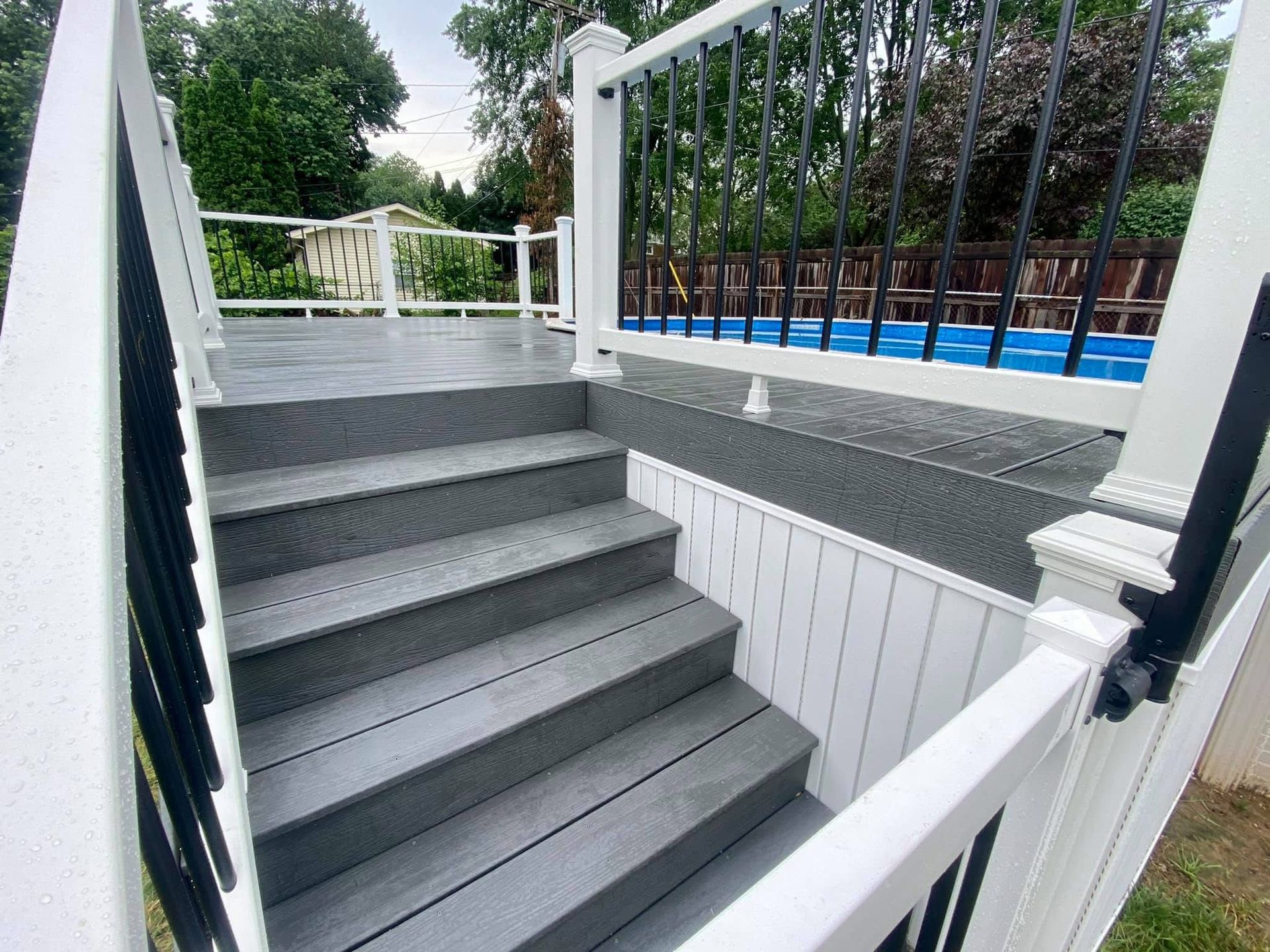 Gray composite deck stairs with black railing and white trim. Blue pool in background.