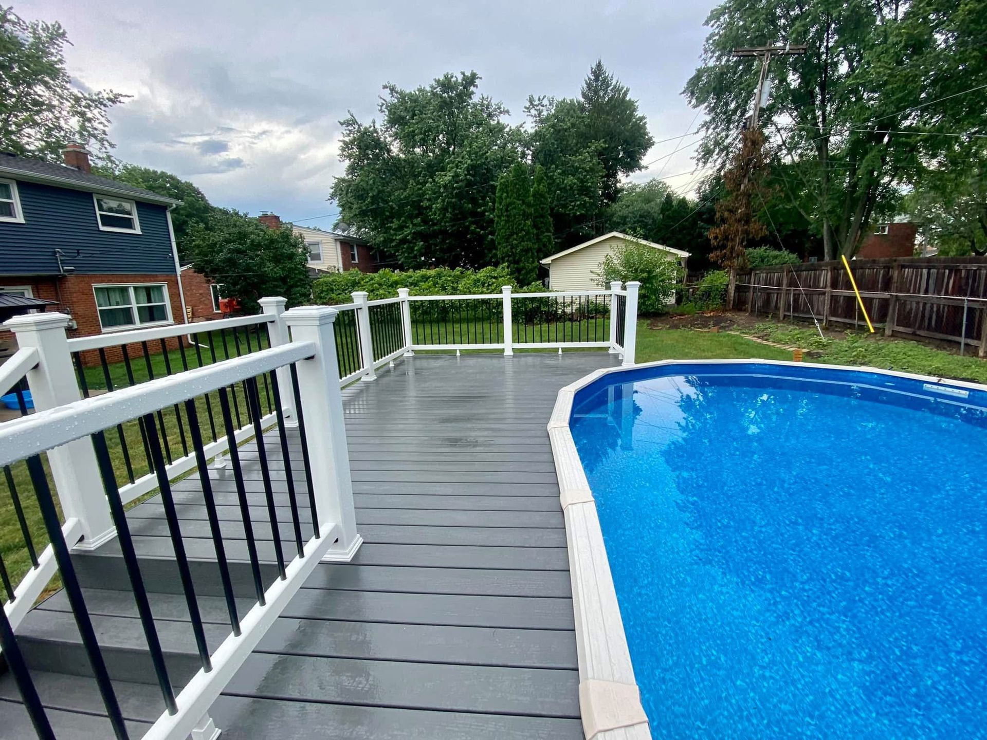 A deck with white railing next to a blue swimming pool in a backyard.