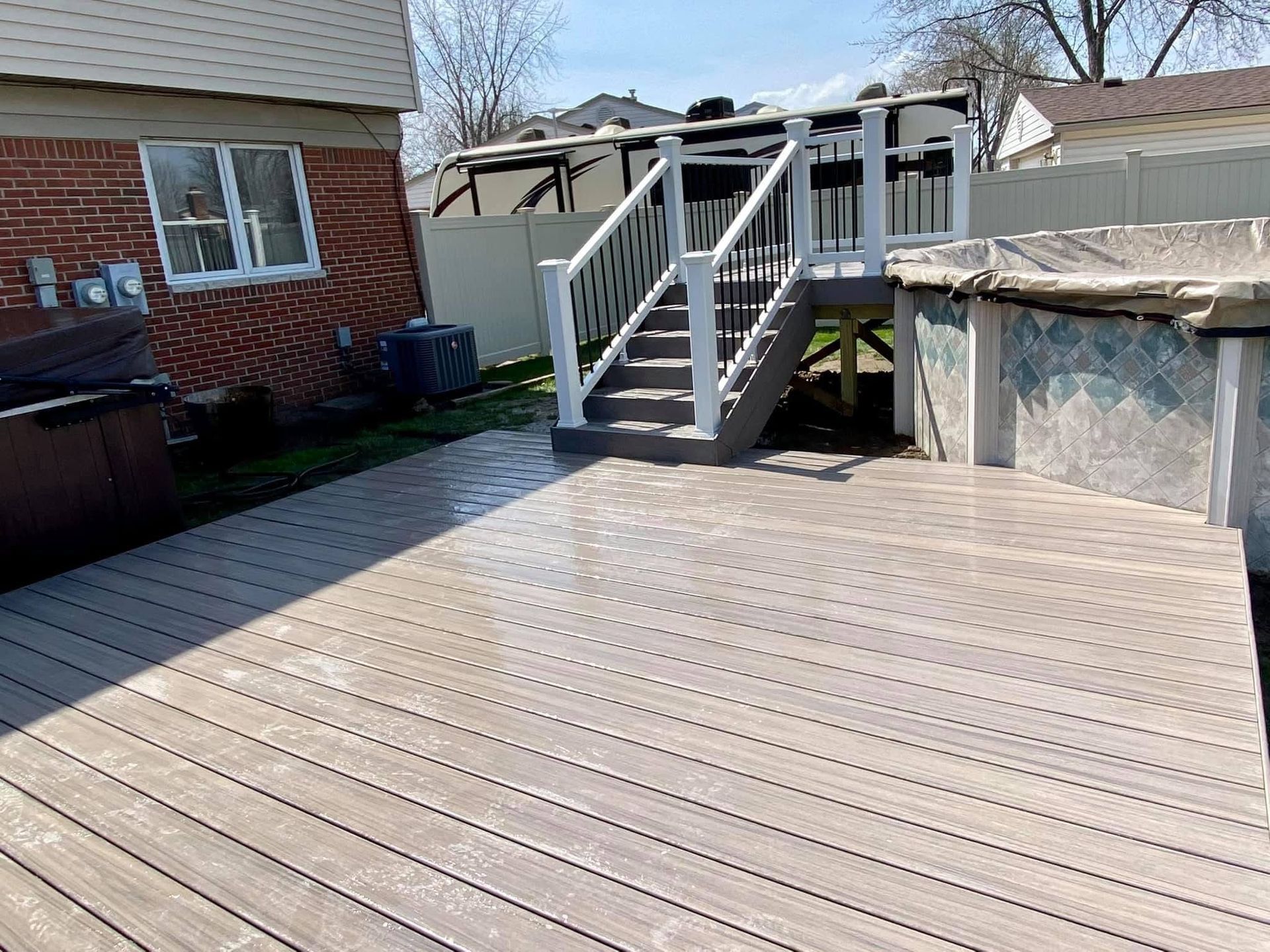 Composite deck with stairs leading up to an elevated structure; hot tub visible.