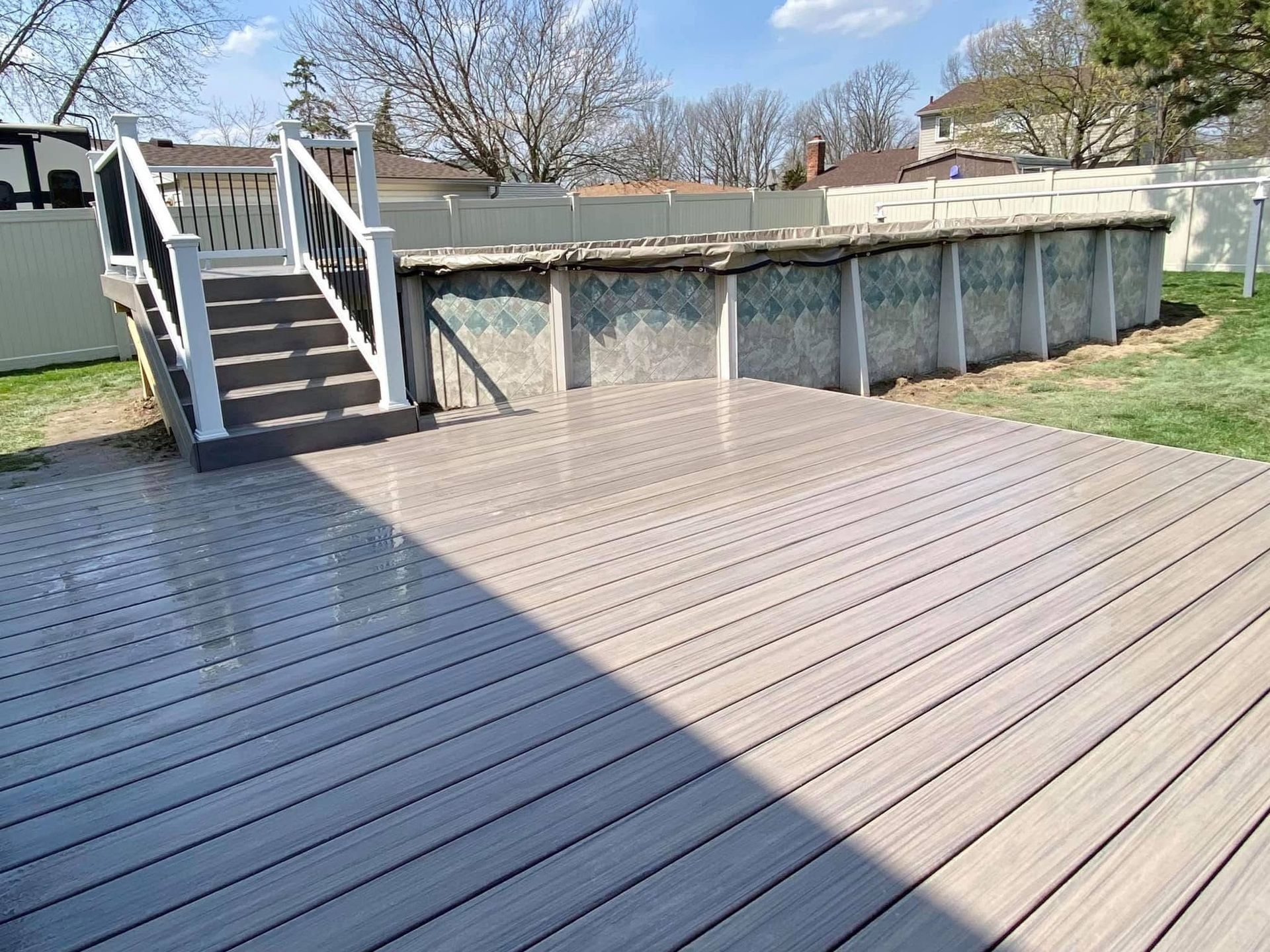 Above-ground pool with composite deck and stairs in a backyard.