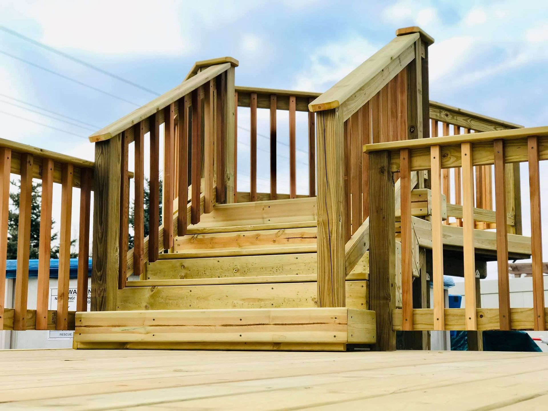 Wooden staircase leading to a deck, featuring railings and steps, set against a cloudy sky.
