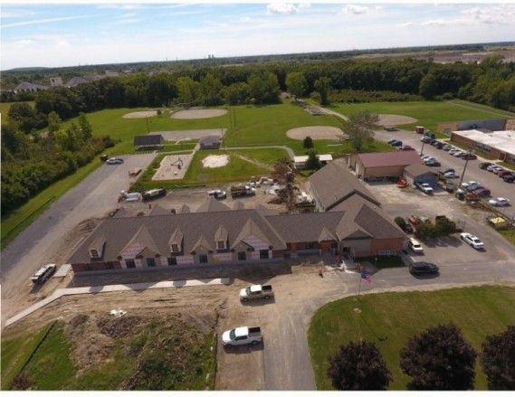 Aerial view of a long, single-story building with a brown roof near a park with baseball fields and a parking lot.