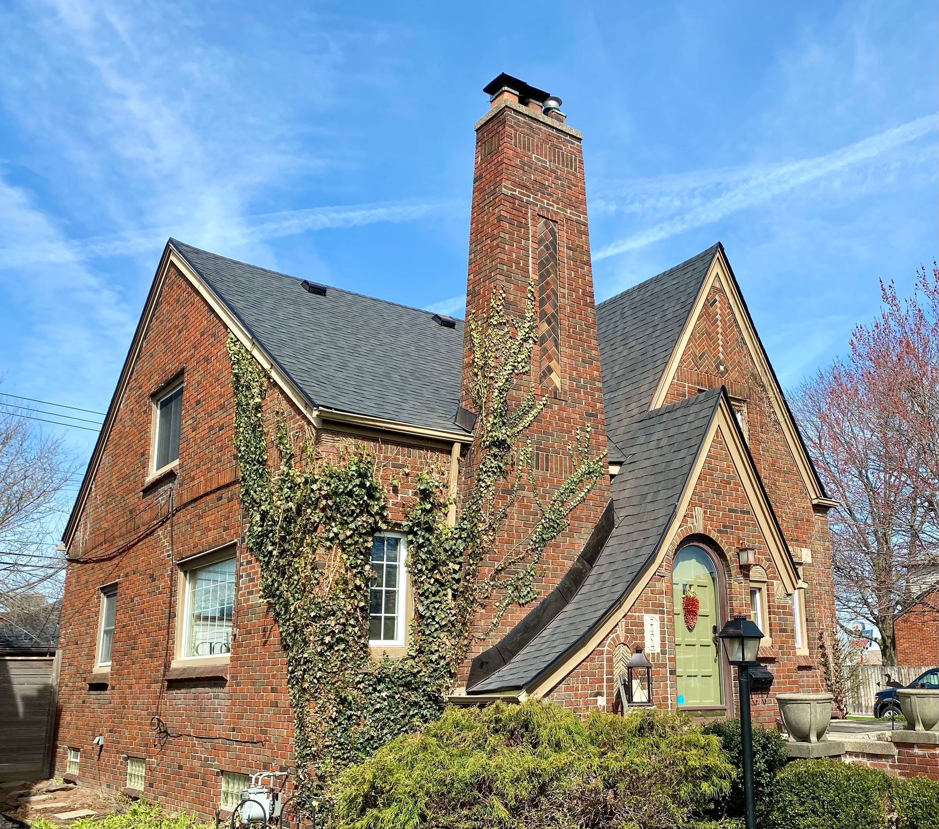 Brick house with dark roof and tall brick chimney. Green door, climbing ivy, and a blue sky.