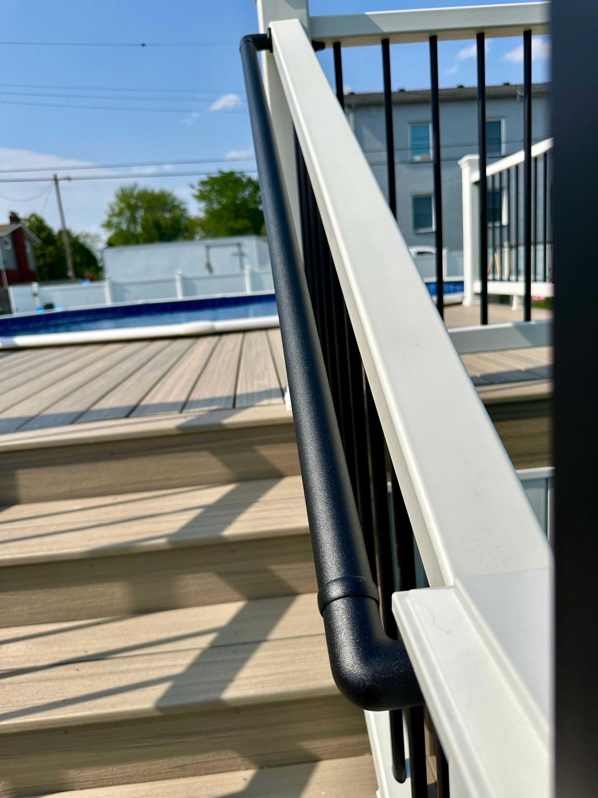 Deck with stairs, white railings, and black balusters. A black, textured handrail is installed.