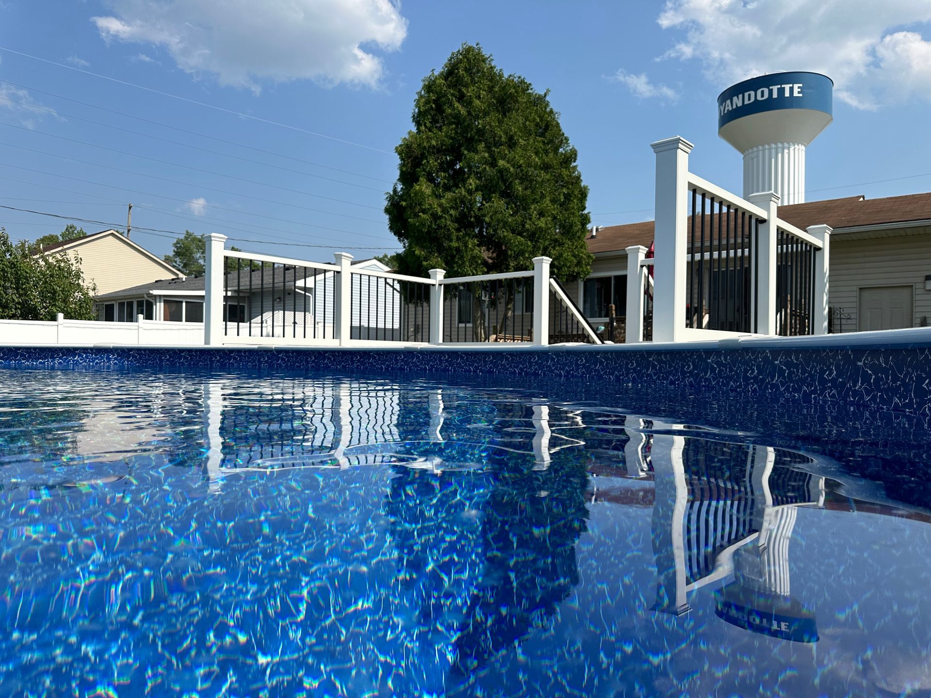 Pool with blue water reflecting a fence, a tree, and a water tower that says 