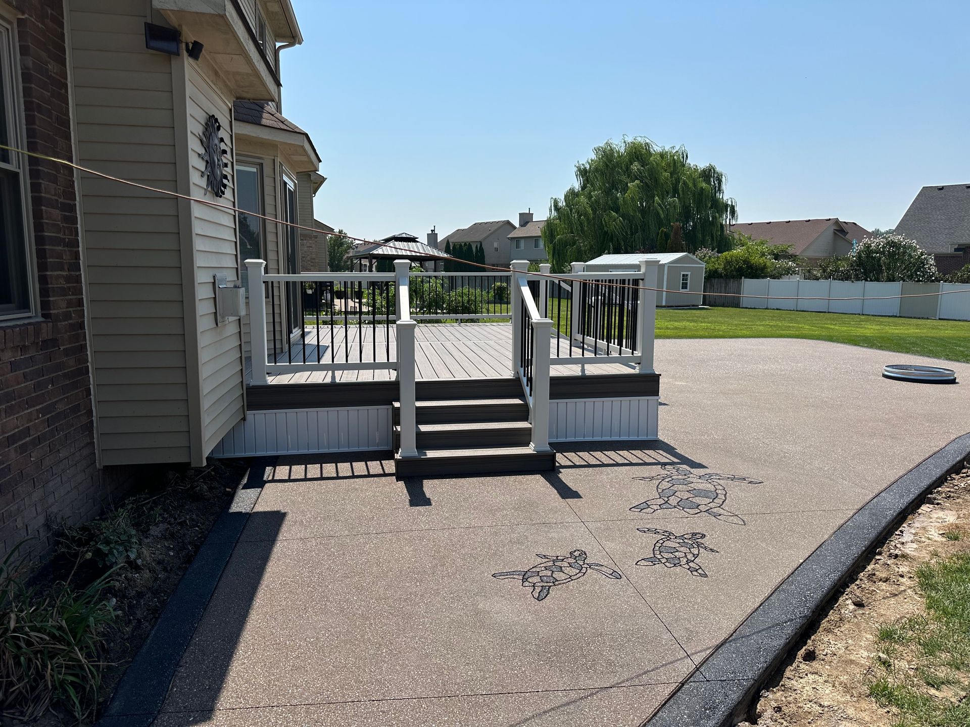 Deck and patio adjacent to a beige house, with steps leading down to a concrete patio.