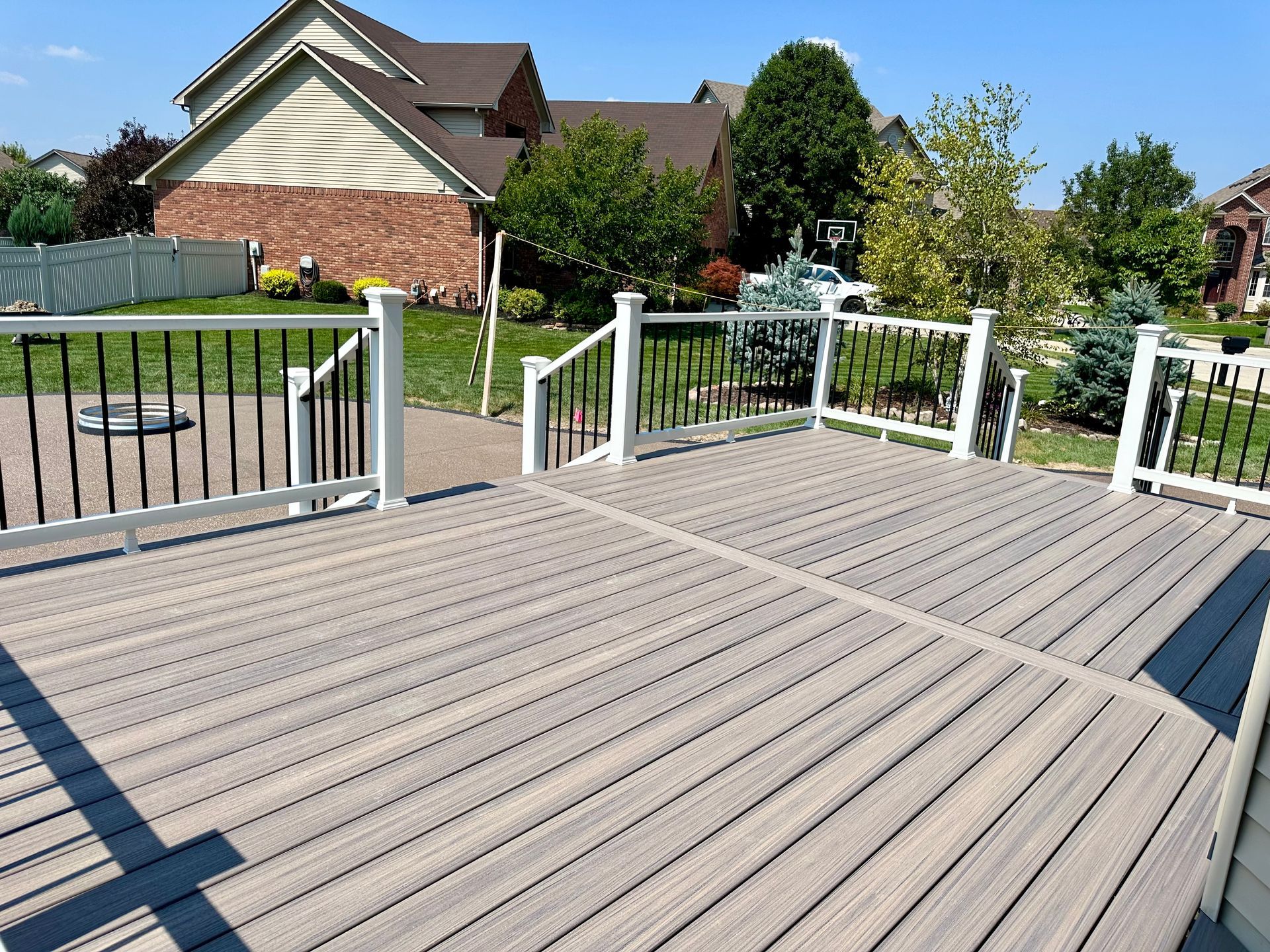 A composite deck with black railings and a white frame, overlooking a residential backyard on a sunny day.