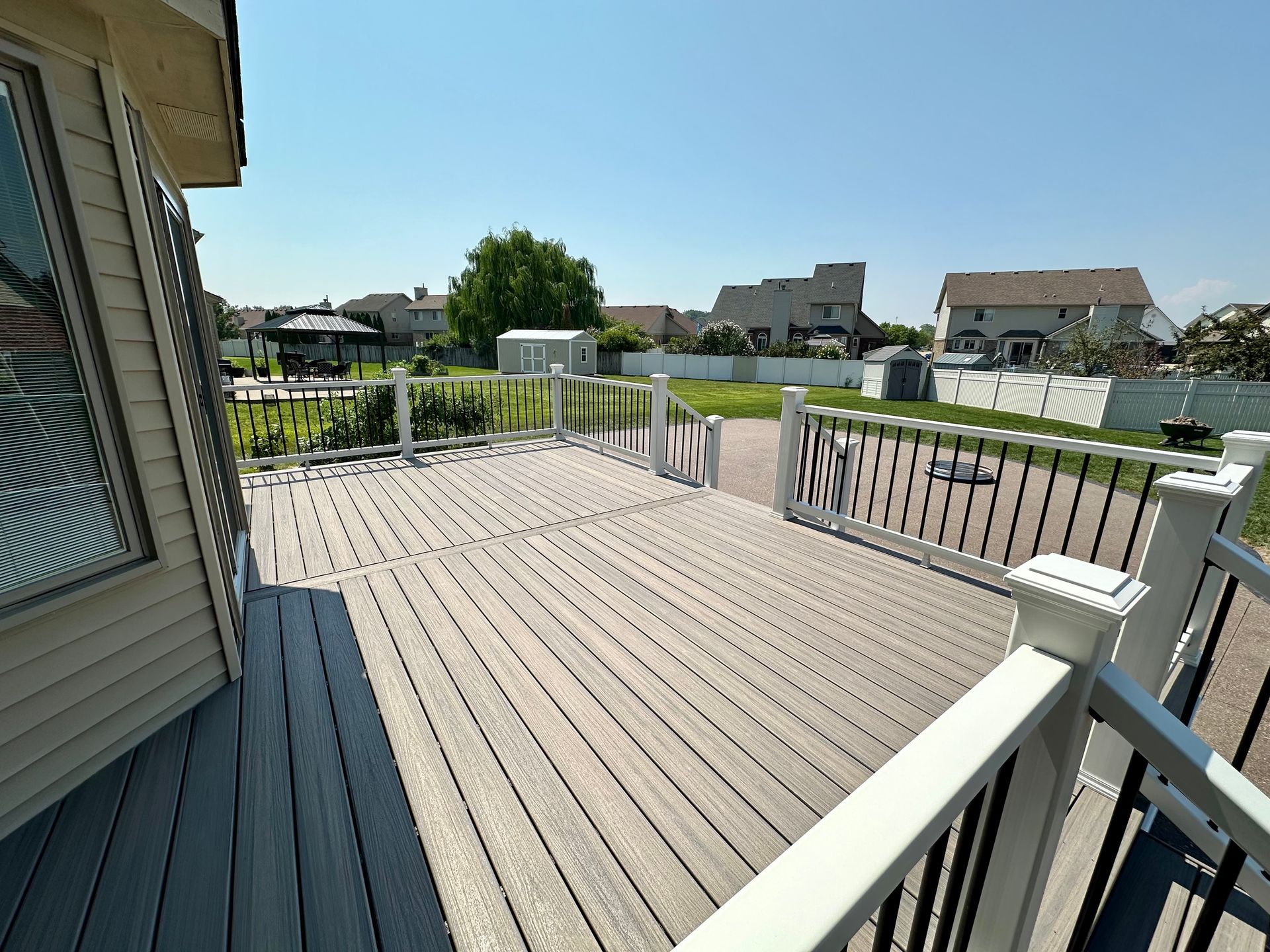 Wooden deck with railings, overlooking a backyard with a gazebo, small shed, and houses.