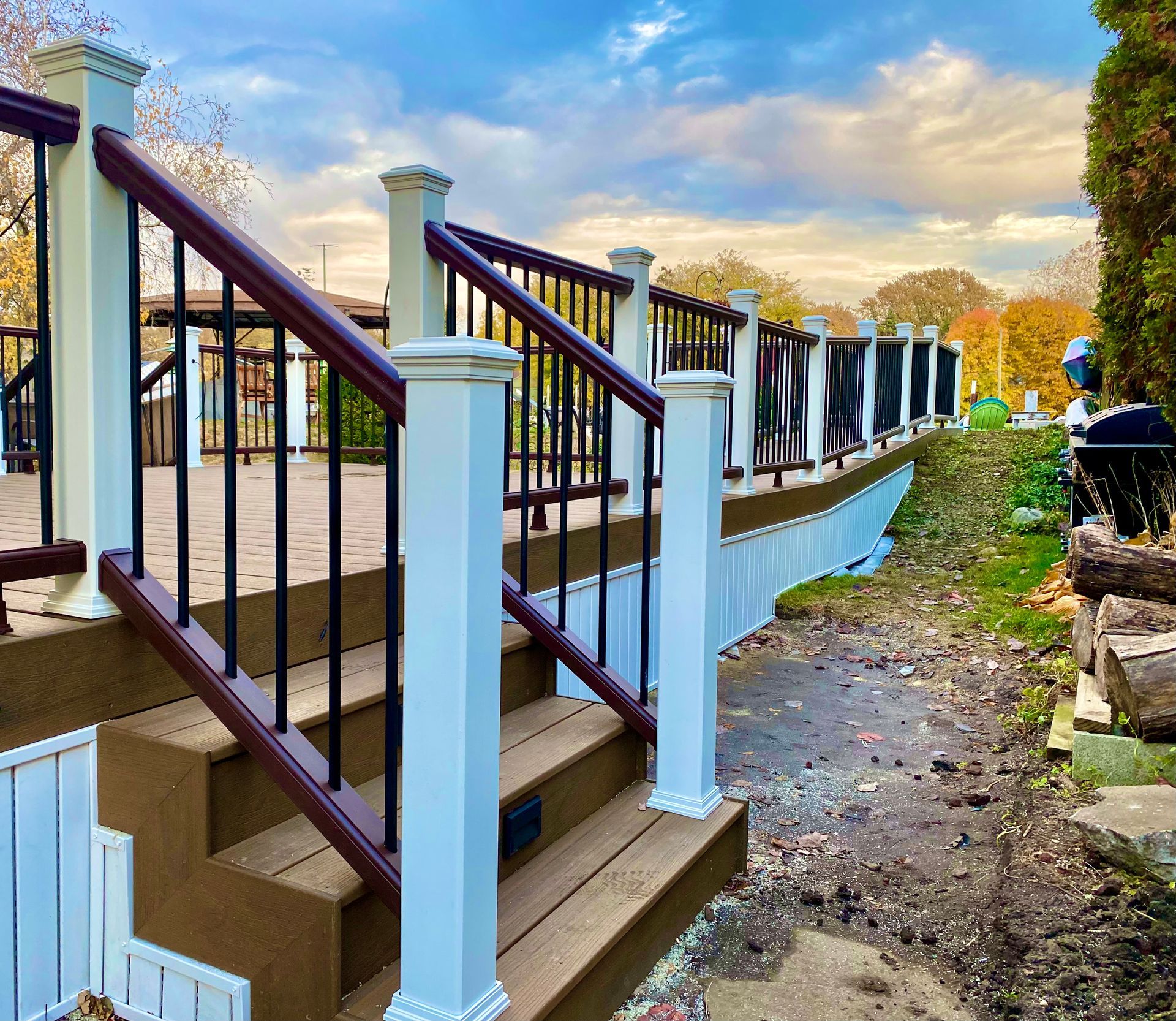 Wooden deck with white posts, brown steps, black railings, and a cloudy sky.