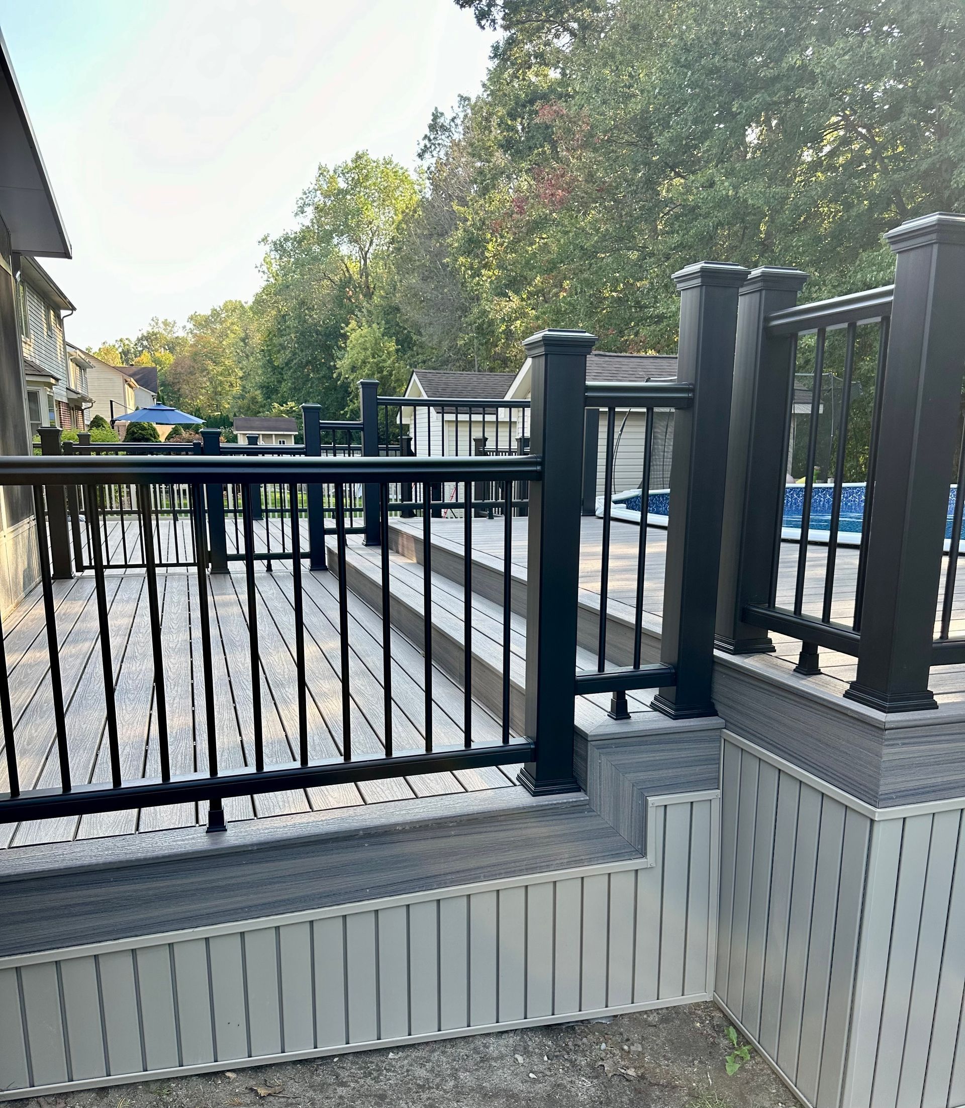 Composite deck with black railing and steps near a pool.