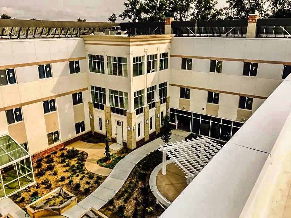 Courtyard of a two-story beige building with windows and a landscaped garden. Includes a pergola and a walkway.