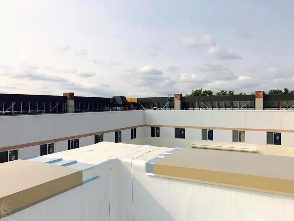 View of a building's white flat roof with white walls, windows, and black barriers against a cloudy sky.