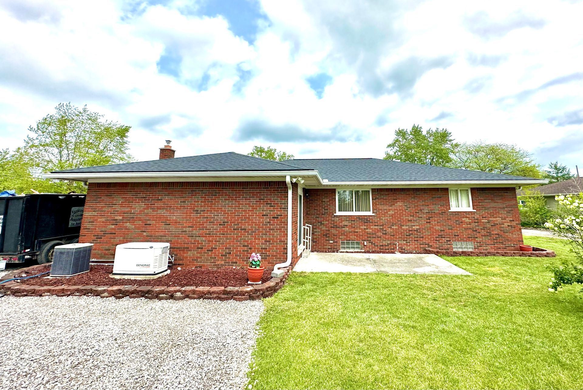 Red brick house with new roof, generator, and green lawn on a cloudy day.