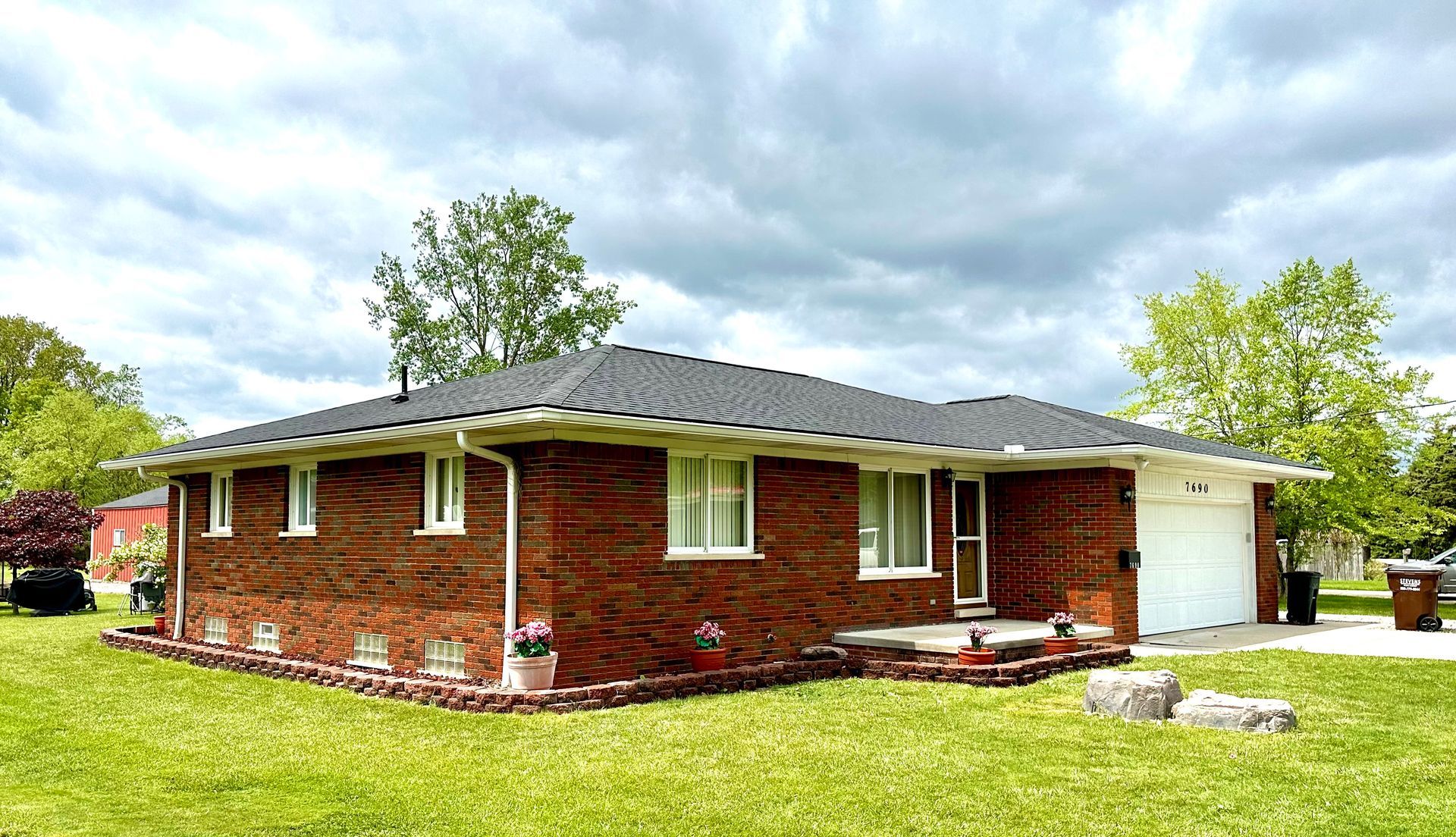 Brick ranch home with a dark roof and attached white garage under a cloudy sky.