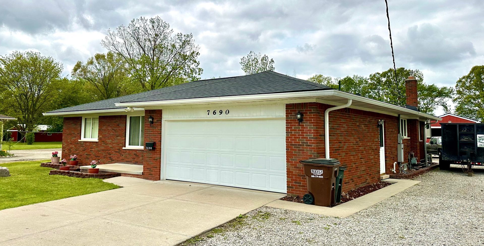 Brick ranch house with a white garage door, concrete driveway, and a cloudy sky.