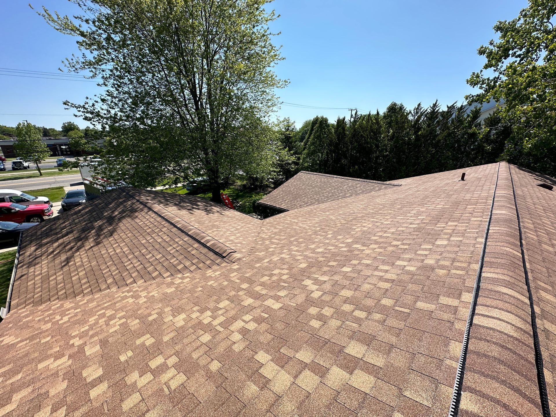 View of a brown shingled roof with trees in the background under a blue sky.