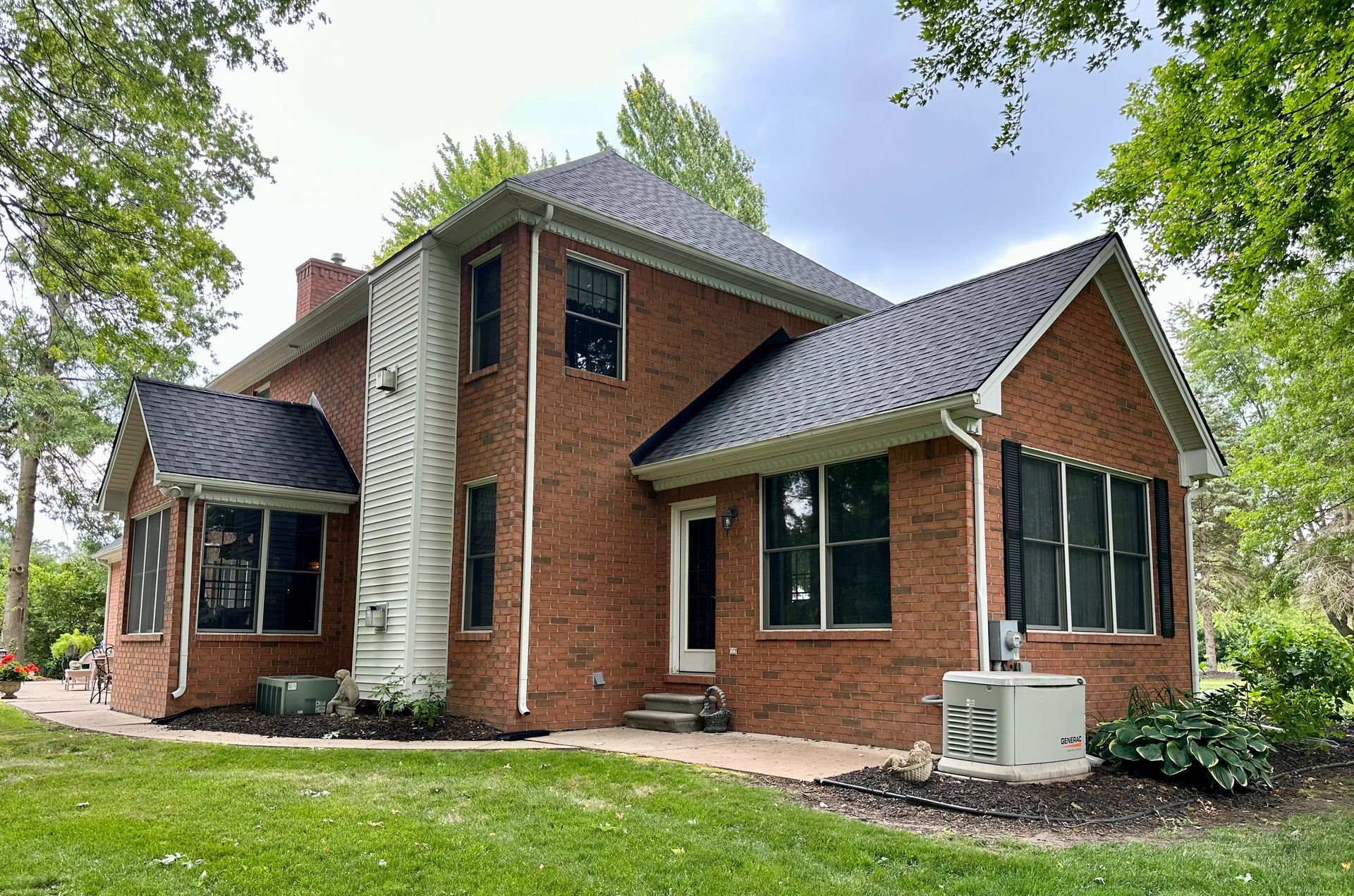 Red brick house with black metal roof, windows, and chimney against a green lawn and trees.