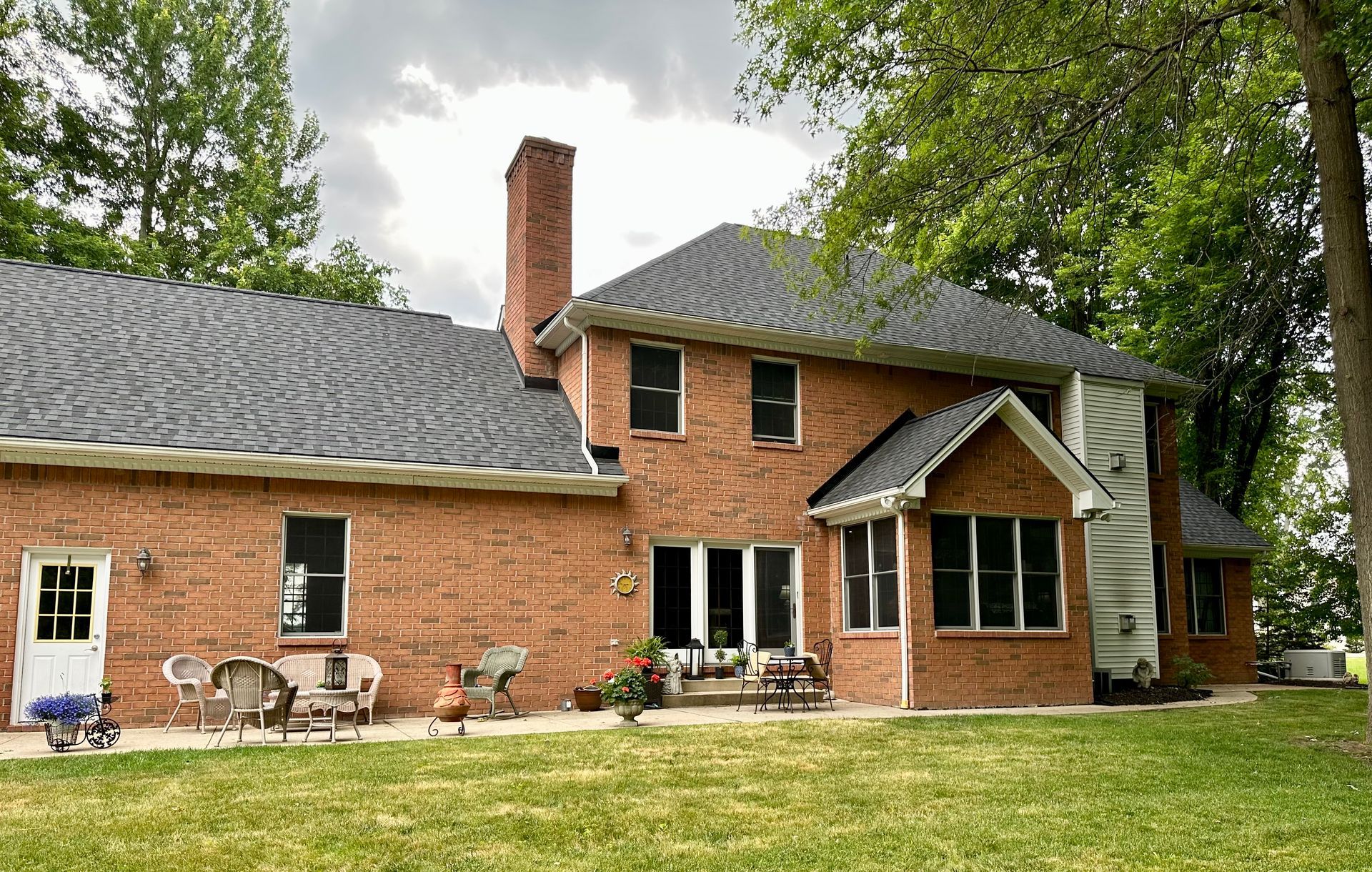 Red brick house with a dark gray roof, chimney, and green lawn.