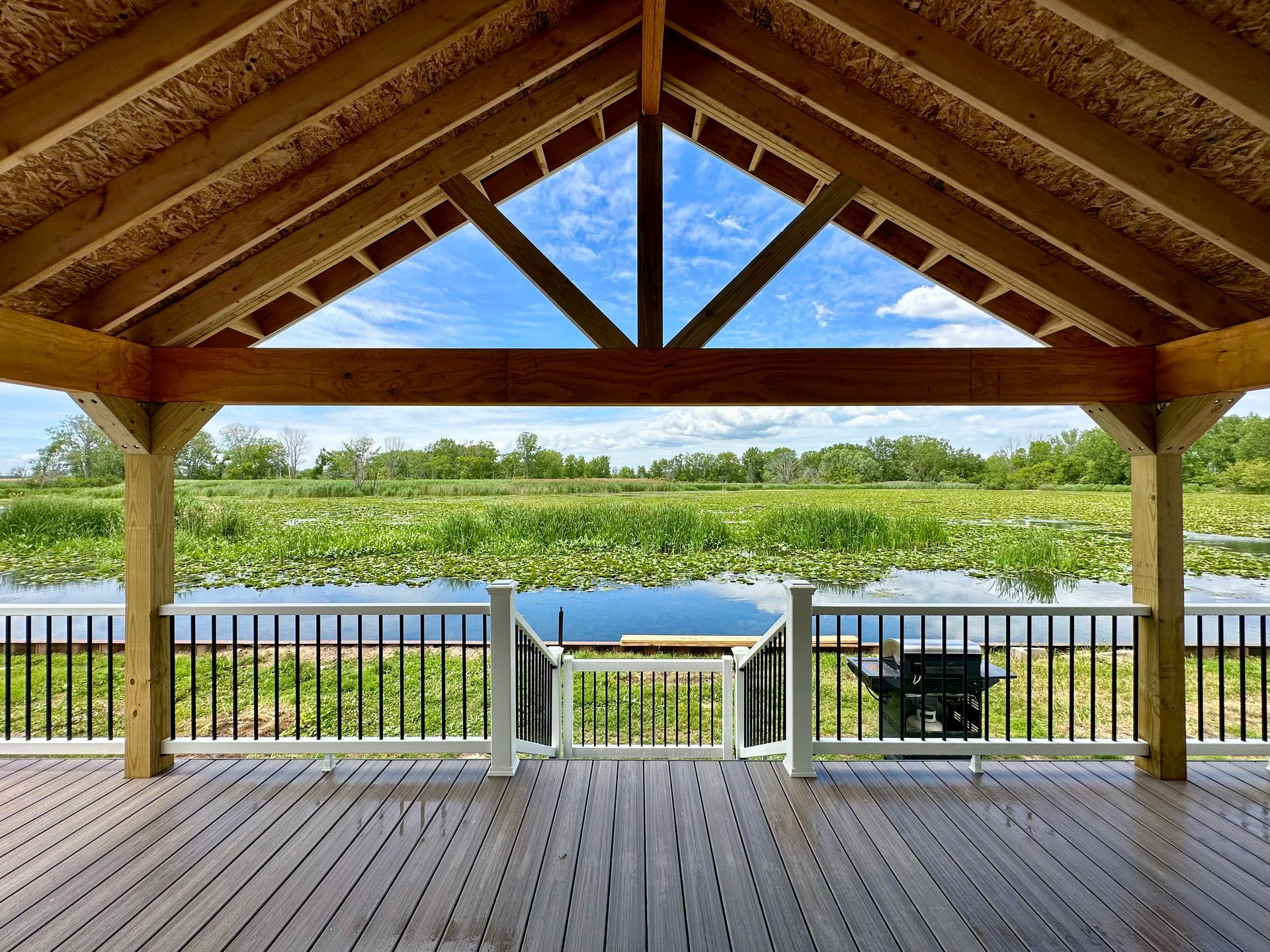 Wooden gazebo overlooking a lake and lily pads, with blue sky in the background.