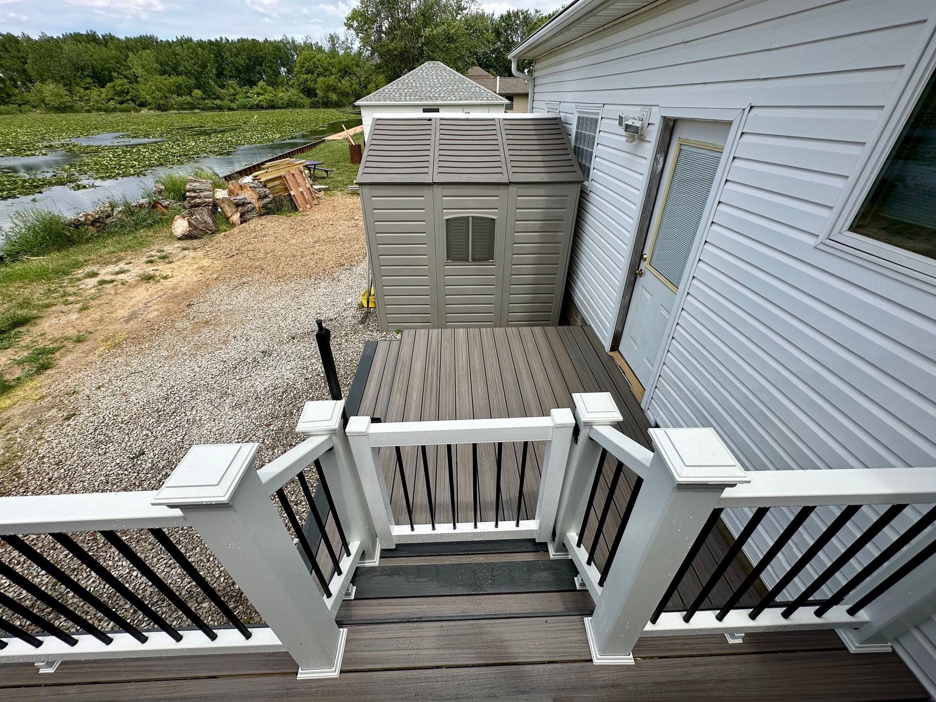 Deck with railing, stairs leading down to a shed and a lake. White house siding to the right.