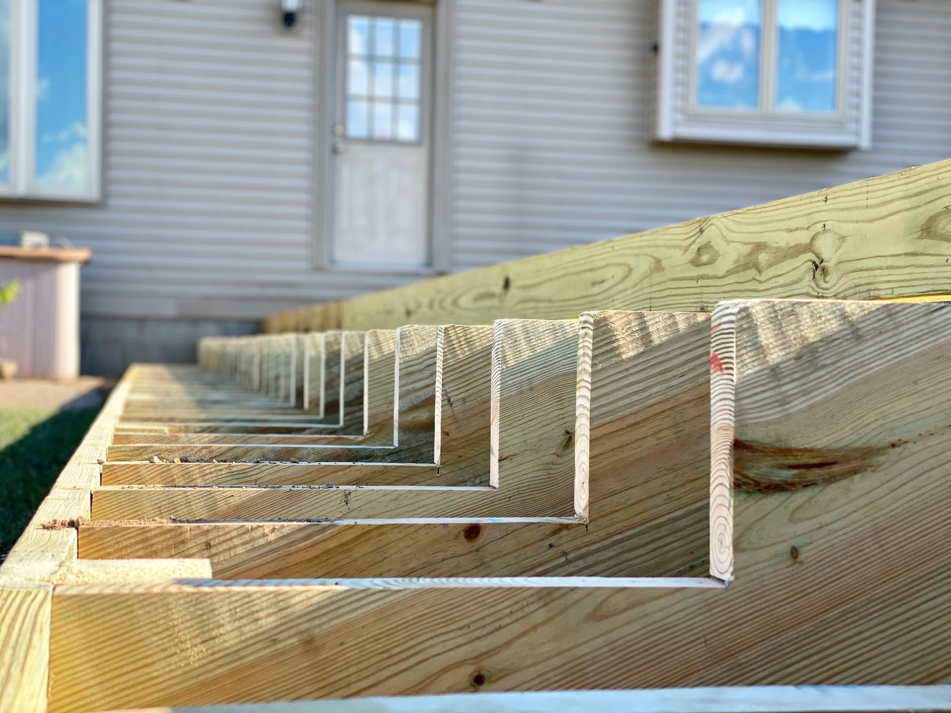 Wooden deck stairs under construction, angled view. Green-treated lumber, light beige house in the background.