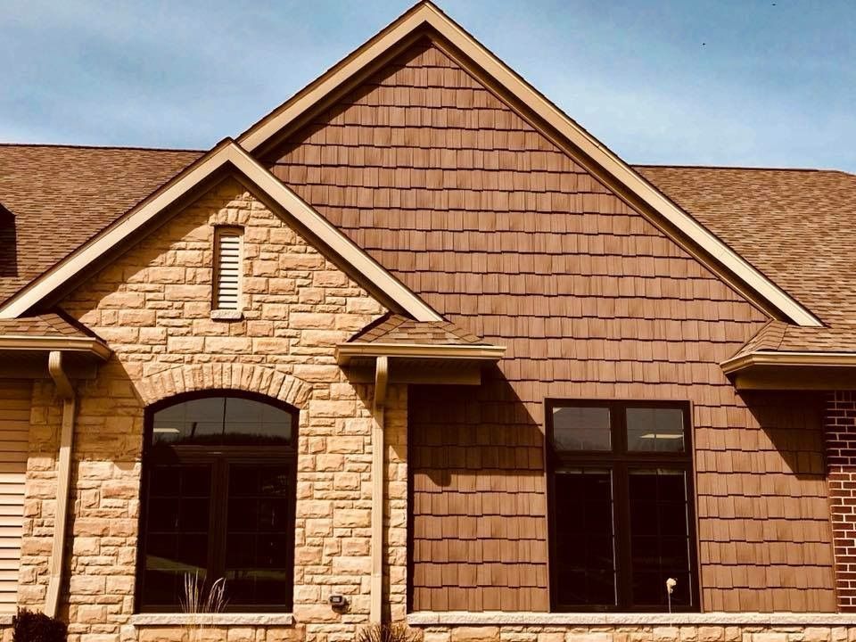Tan and brown brick and shingle home exterior with dark windows and gabled roof.