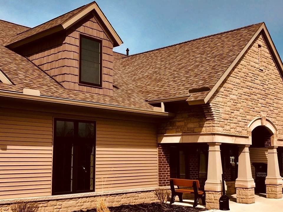 Tan building with brown roof, stone facade, and dark window frames.