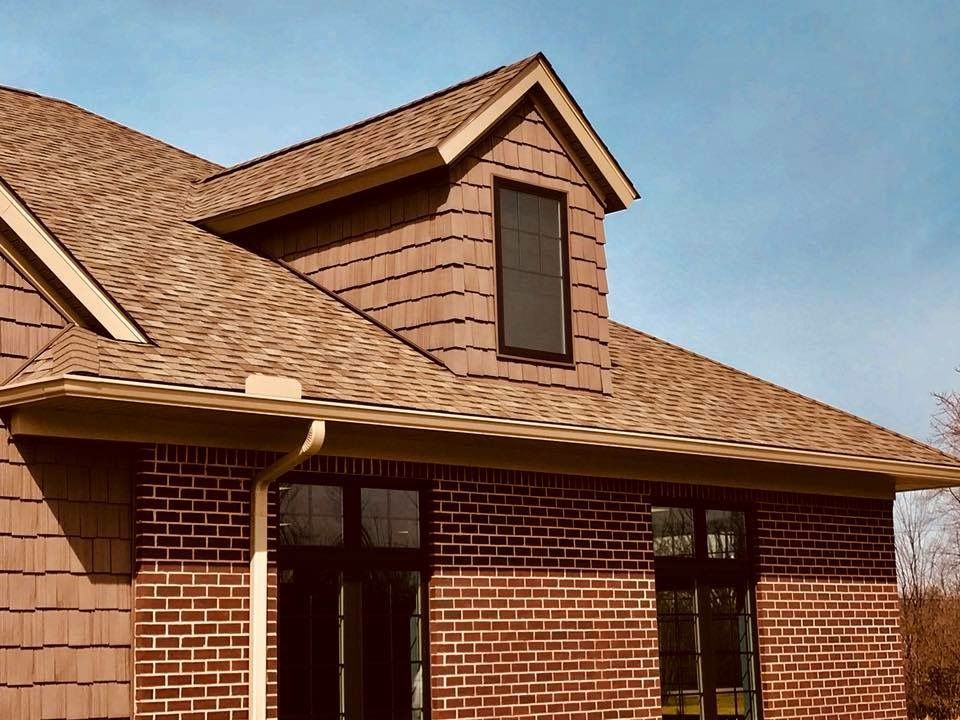 Brick house with brown roof and dormer, under a blue sky.