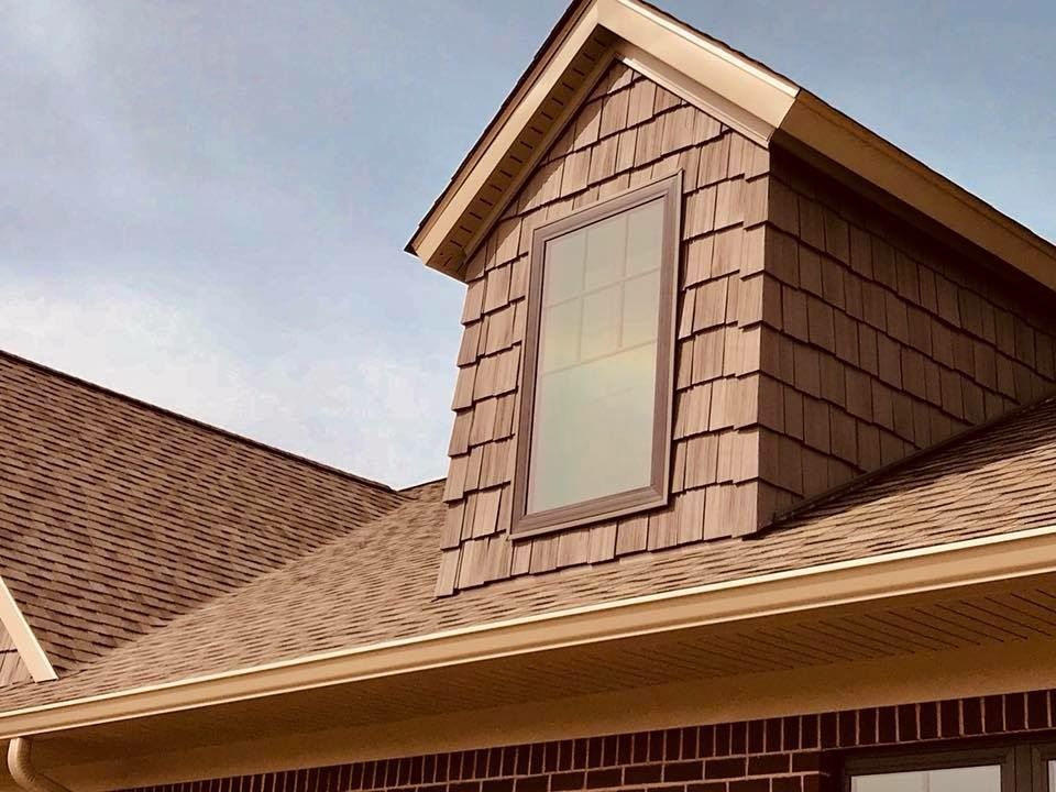Brown shingle roof with a dormer window, brown trim, and brick siding.