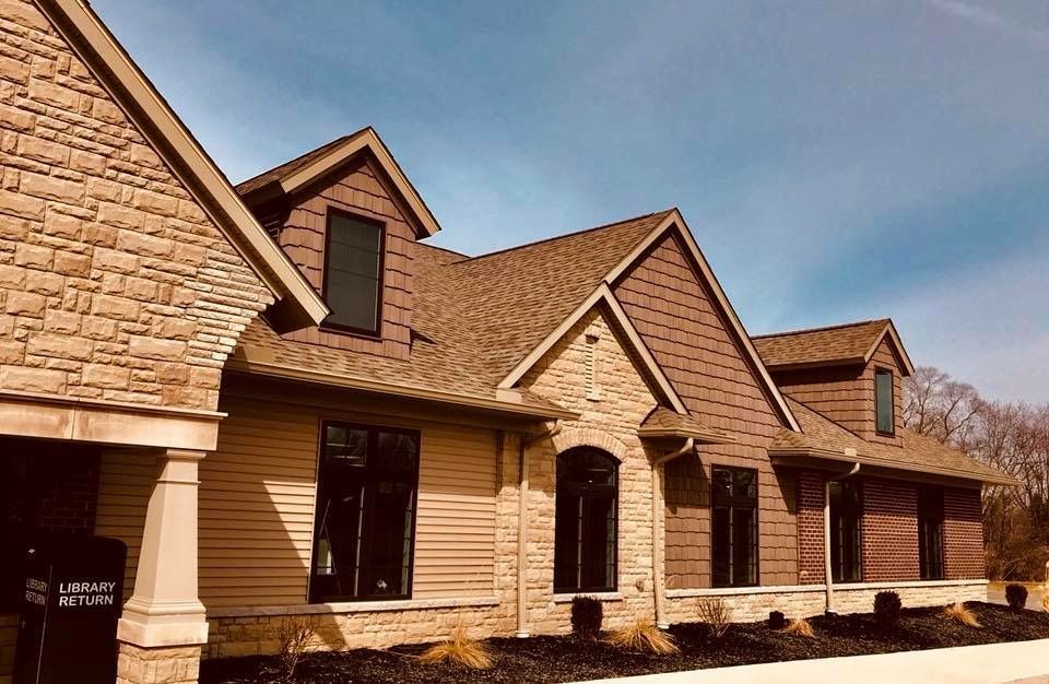 Tan and brown brick and siding building with a dark roof and windows under a blue sky.