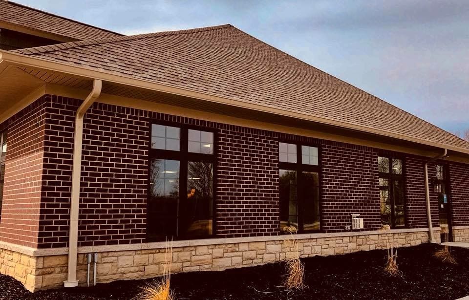 Brick building with brown roof, beige trim, and dark-framed windows.