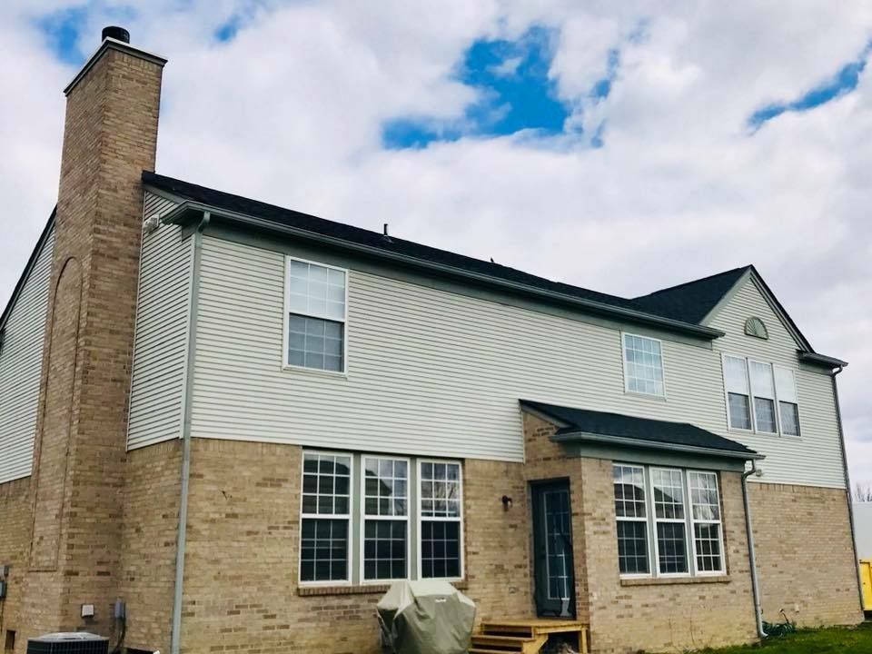 Two-story house with brick and siding exterior, dark roof, chimney, windows, and a cloudy sky.