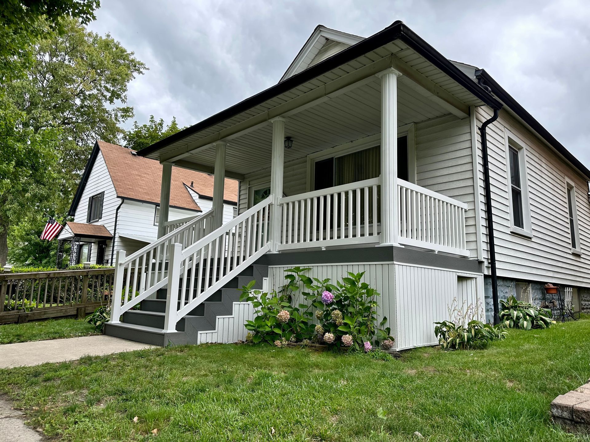 White house with porch and steps, gray trim, and green lawn on a cloudy day.